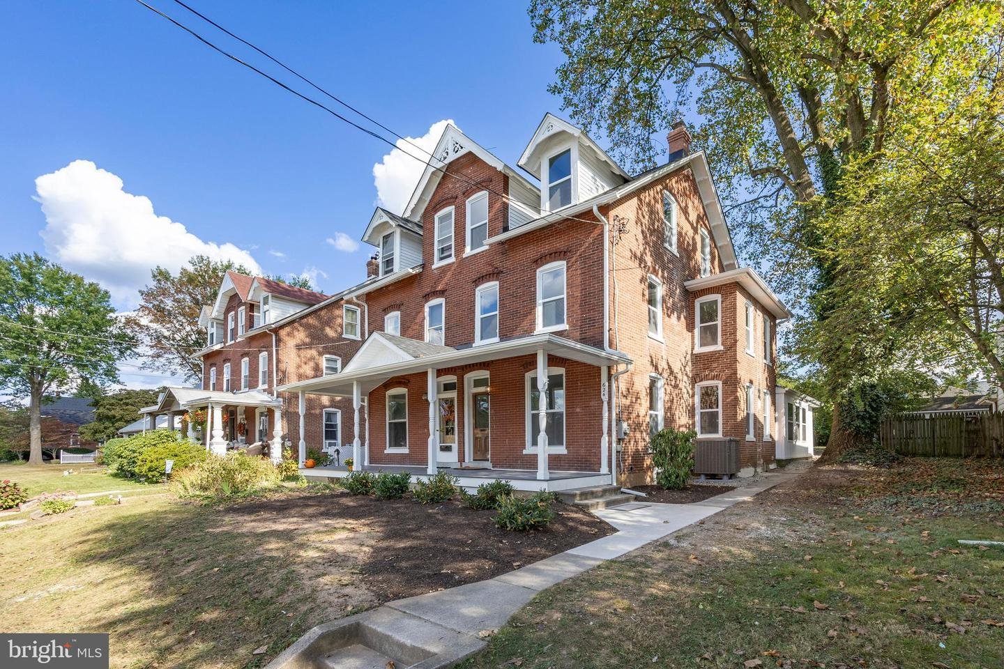 Historic red brick Victorian-style house with white trim and porch, surrounded by trees and a grassy yard under a blue sky.