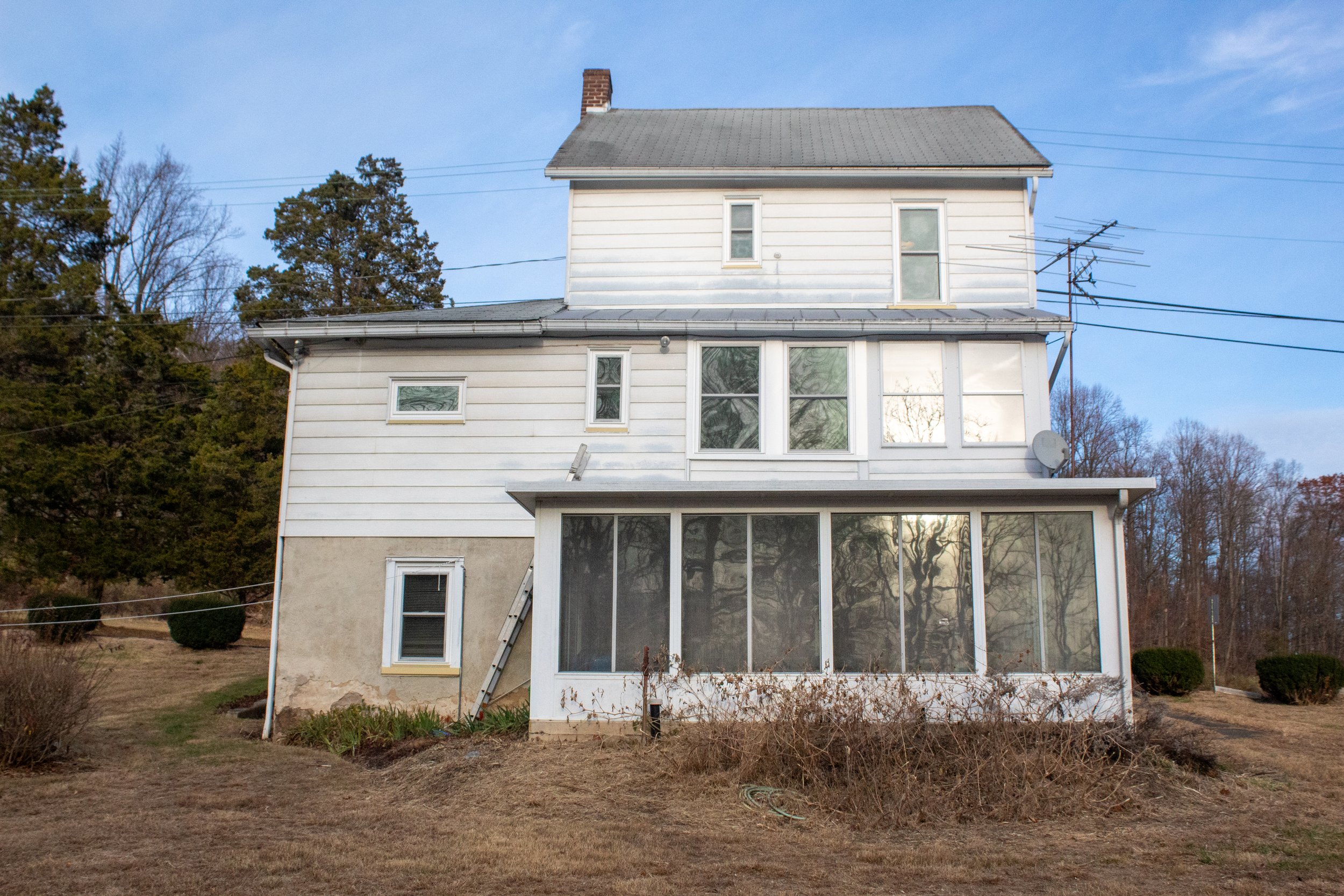 Two-story white house with a gray roof and a small, enclosed porch facing forward, situated on a grassy lawn.
