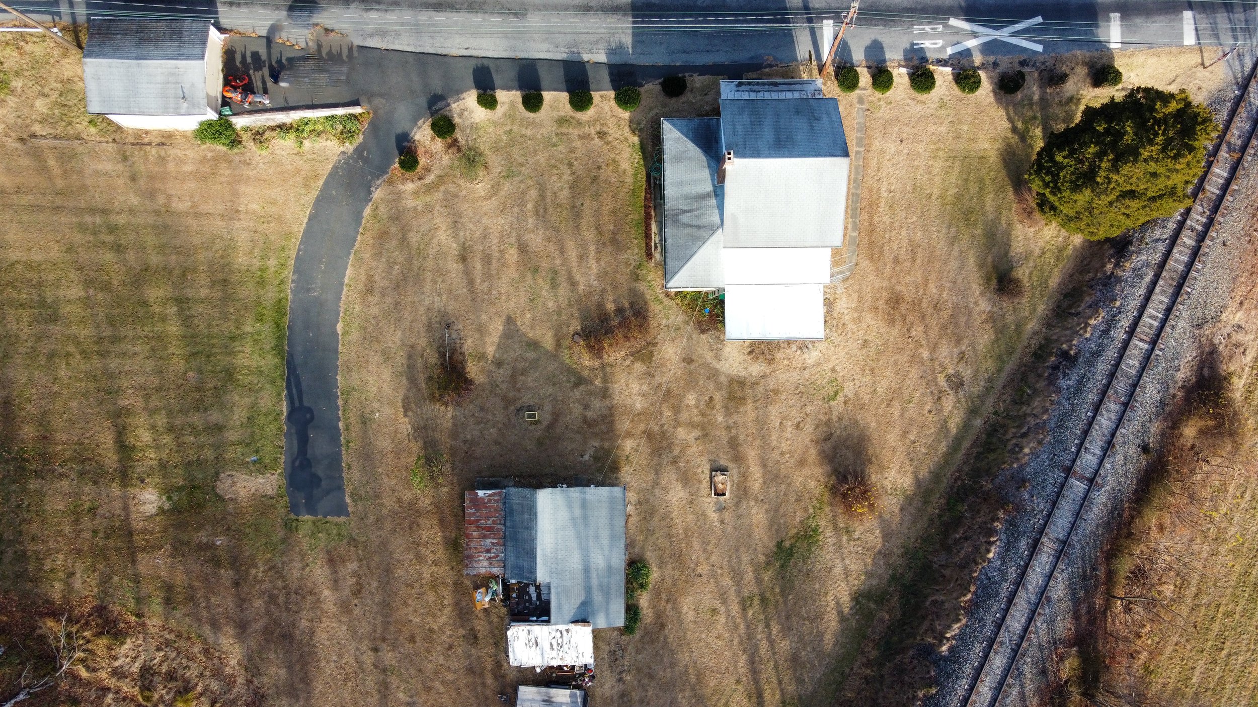 Aerial view of a rural landscape with a house, shed, driveway, and adjacent railroad tracks.
