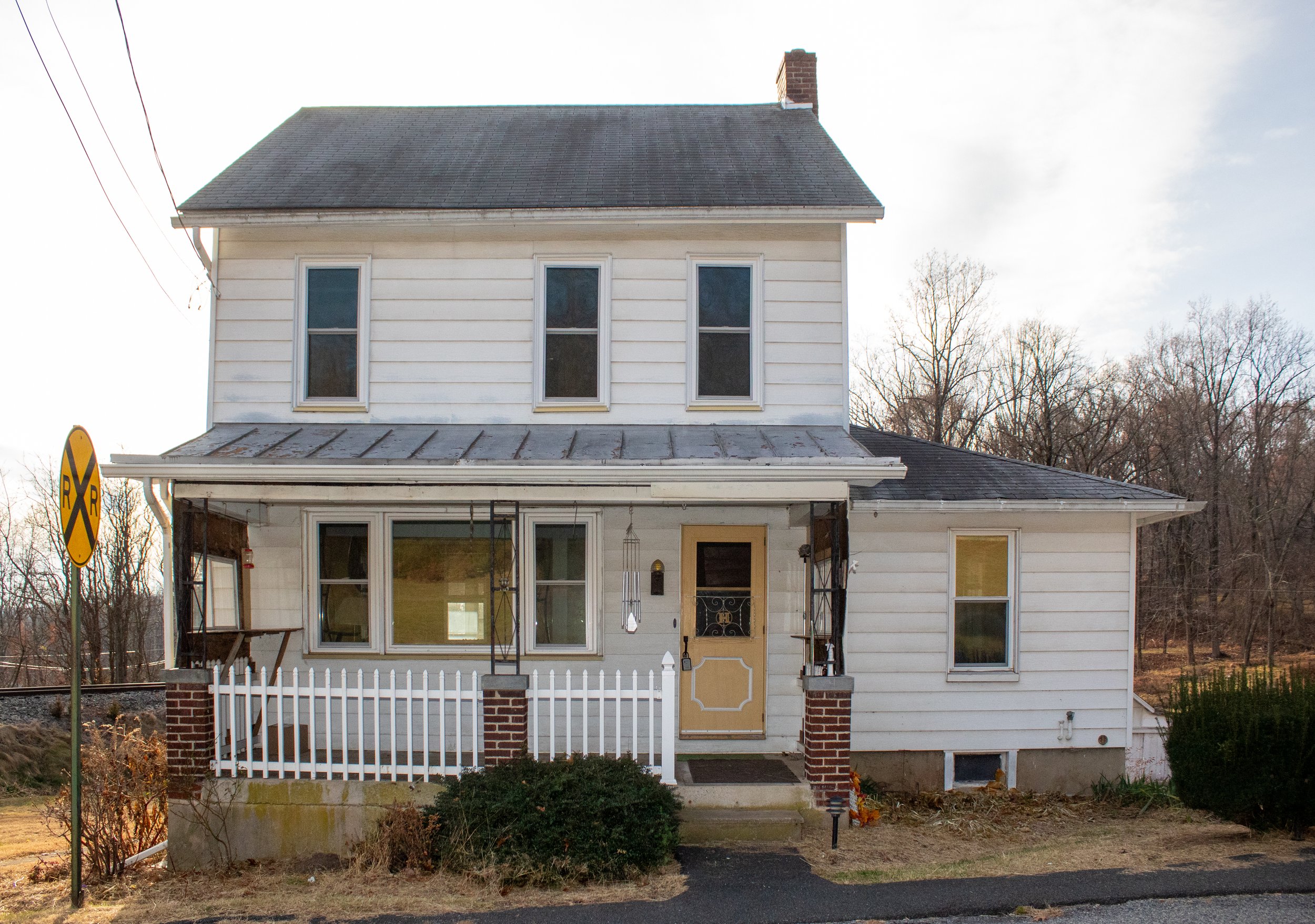 Old white house with a porch and a railroad crossing sign