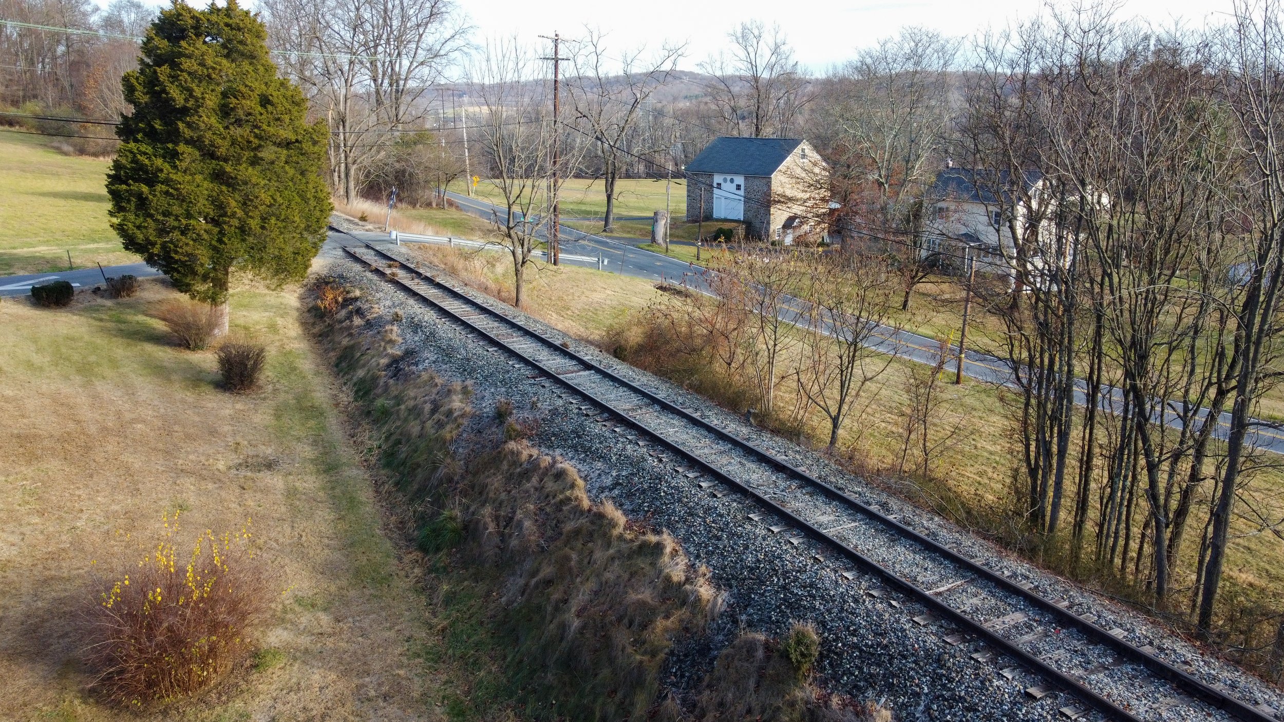Railroad tracks running through a rural landscape with trees, grass, and a small stone building beside a road.