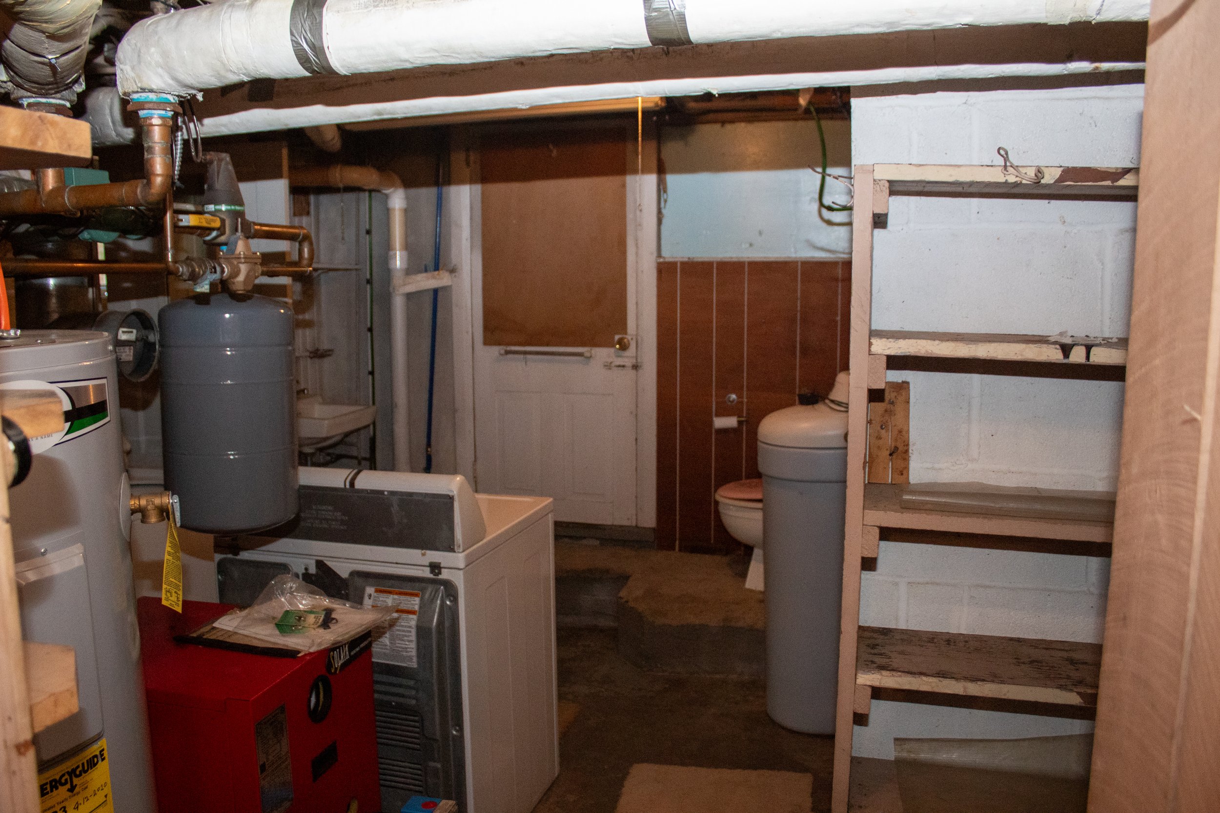 Basement with laundry area, water heater, pipes, shelves, and a toilet