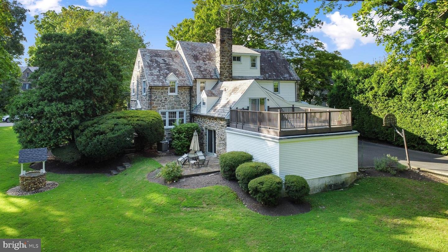 Stone house with a shingled roof, large patio, and surrounding green lawn and trees.
