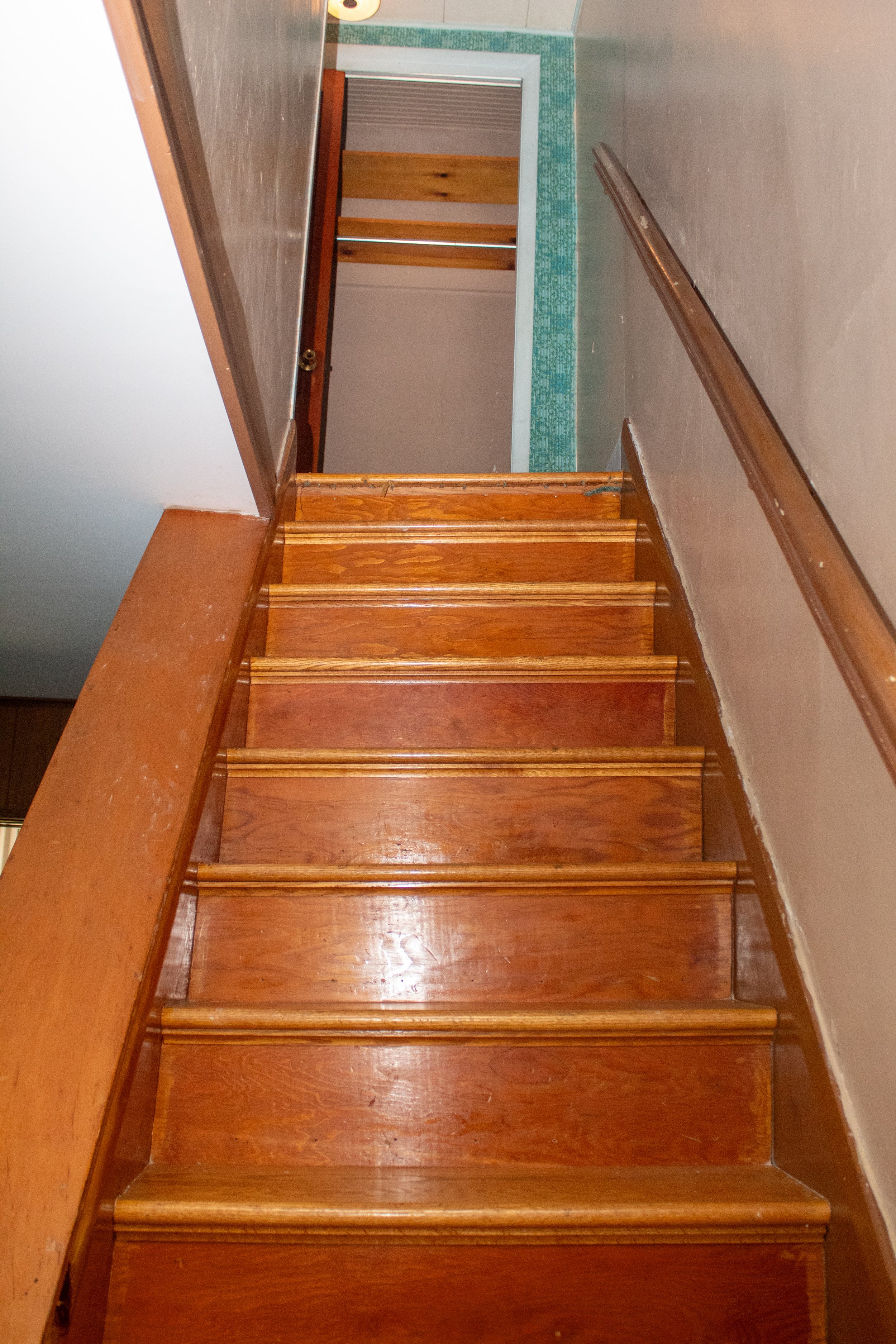 Wooden staircase leading upwards with handrails on both sides, ending at an open doorway.