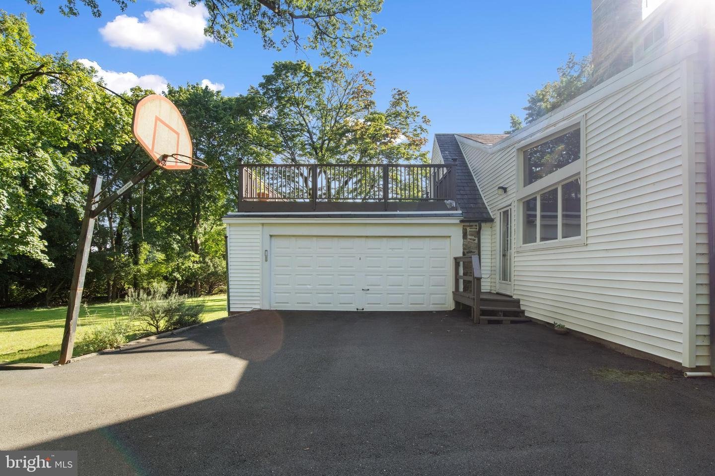 Driveway with basketball hoop and garage, surrounded by trees.