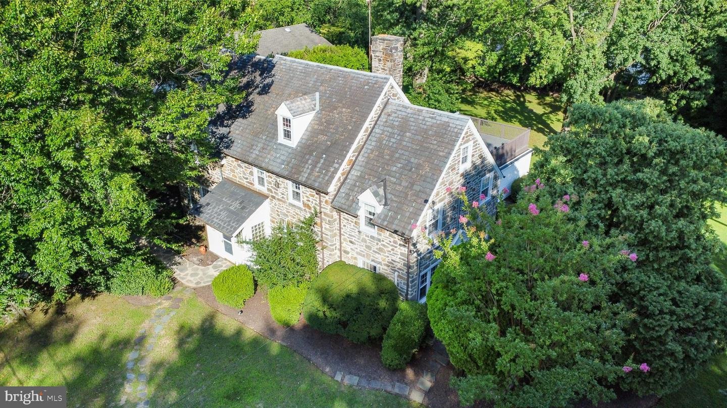 Aerial view of a large stone house surrounded by lush green trees and a well-maintained garden.