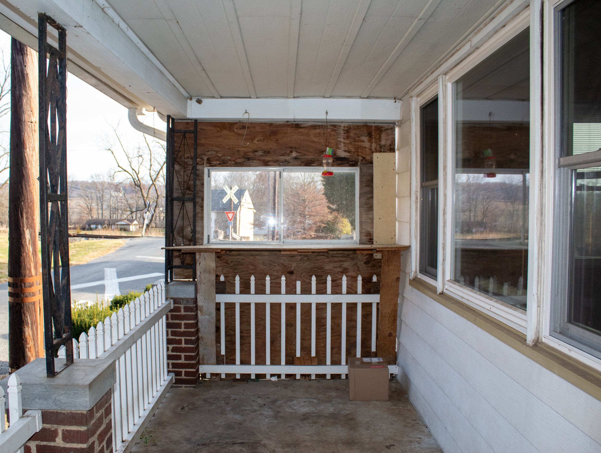 A porch with wooden railings and large windows, view of outdoor road and trees.