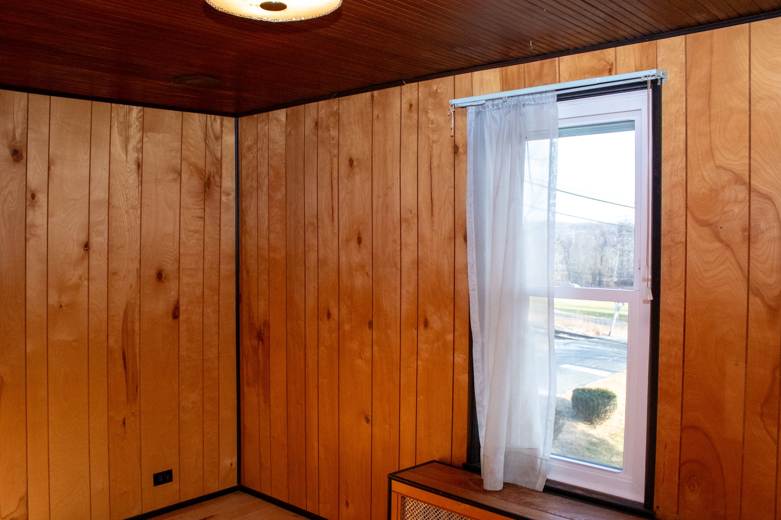 Interior room with wood paneling and a window with a sheer curtain.