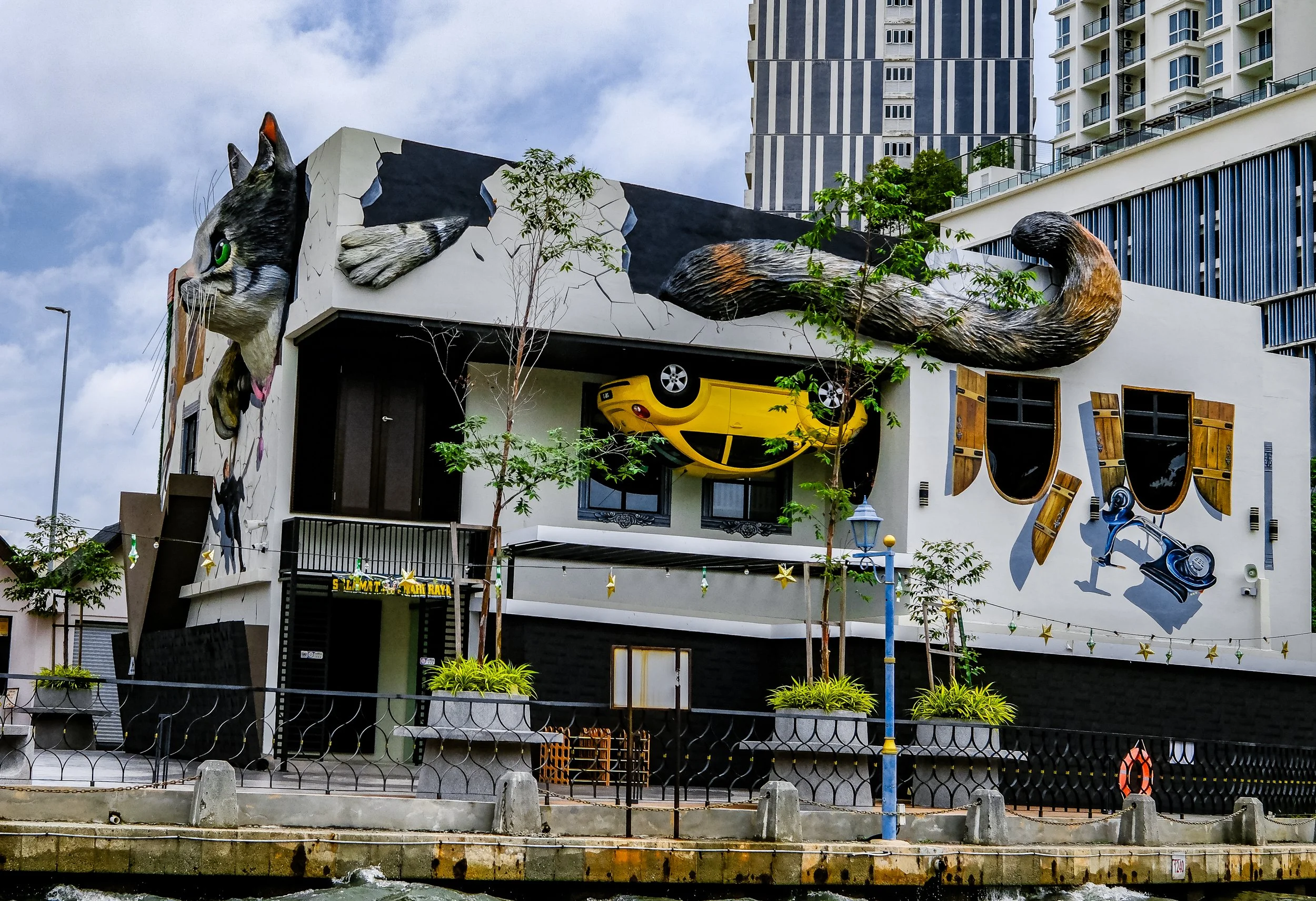 Building with colorful murals of a cat, a toy car, and a robot on the exterior wall, with small trees and street furniture in front.