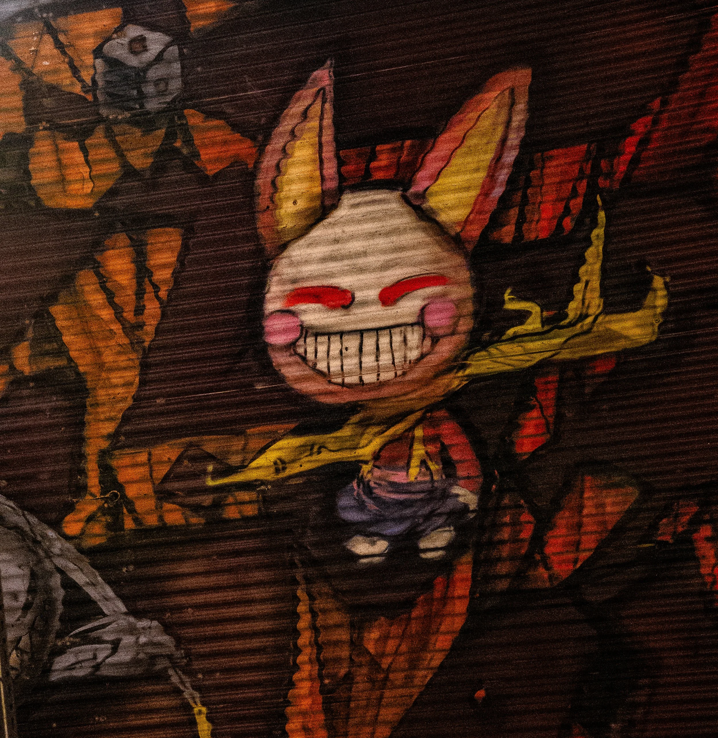 Colorful graffiti of a smiling cartoon character with bunny ears, red eyebrows, and pink cheeks, surrounded by abstract shapes and patterns.