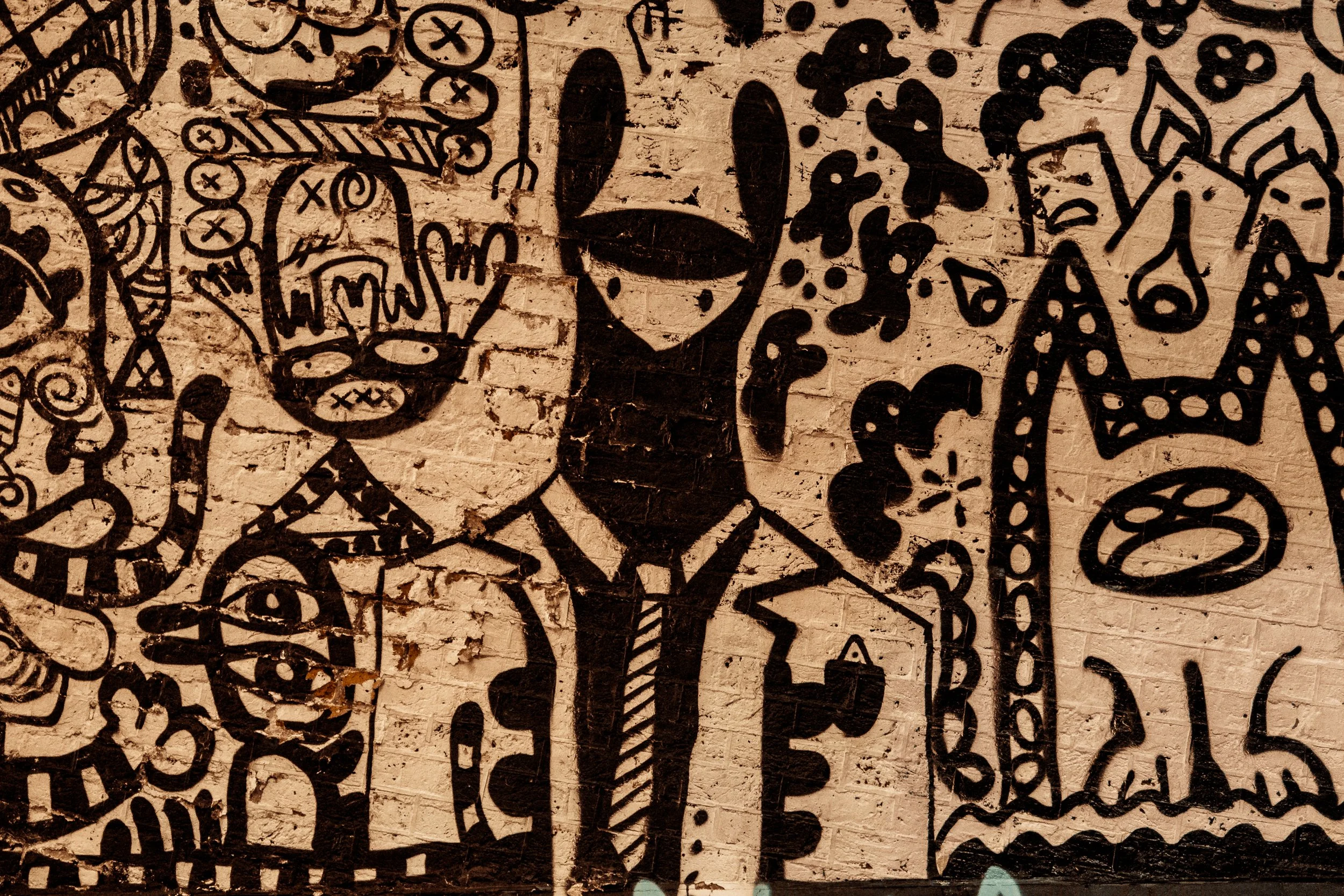 Black graffiti of a person wearing a hat and tie on a brick wall, surrounded by various abstract designs and patterns.