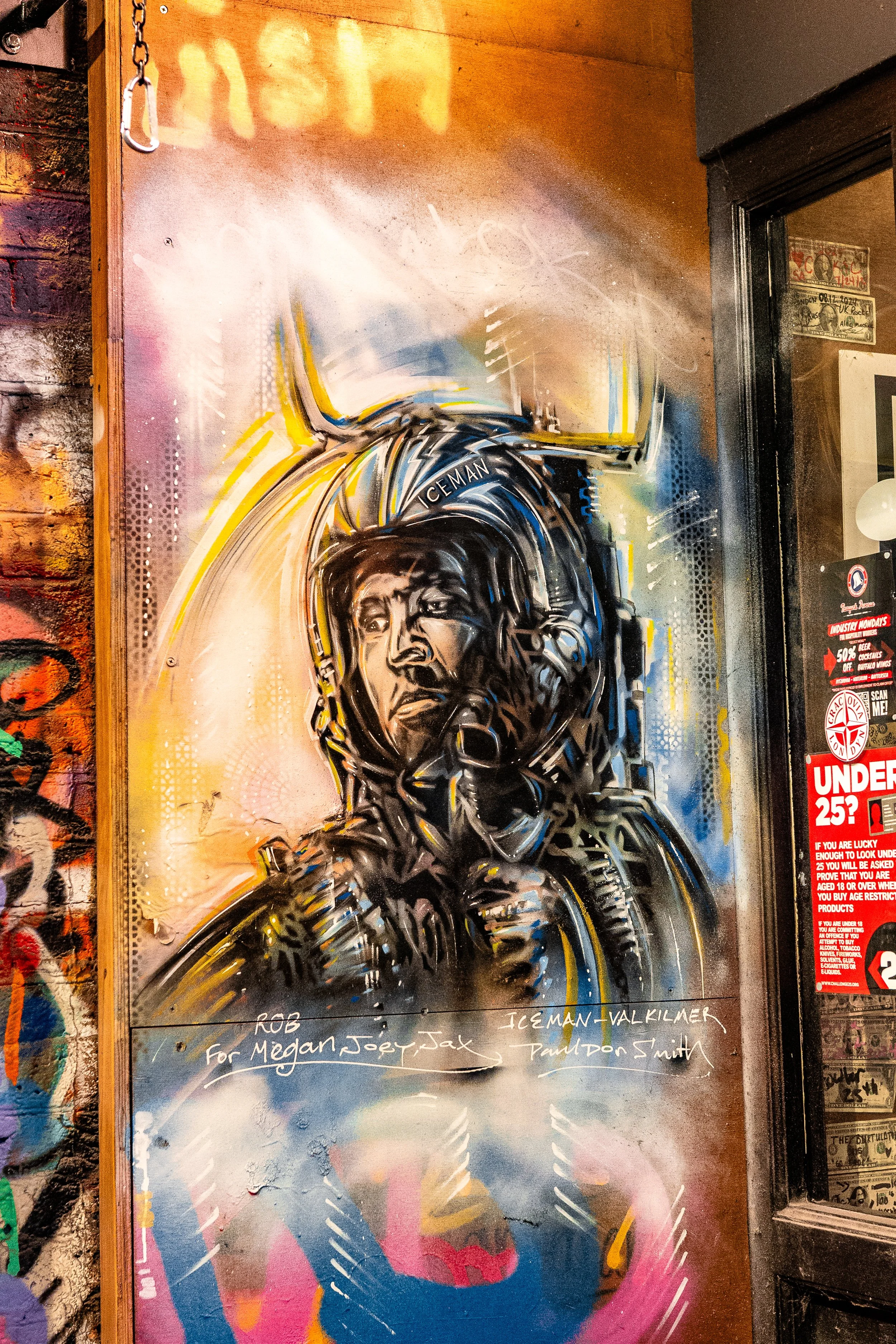 Graffiti mural of an astronaut with a serious expression, wearing a helmet and space suit, with vibrant colors and abstract background elements.