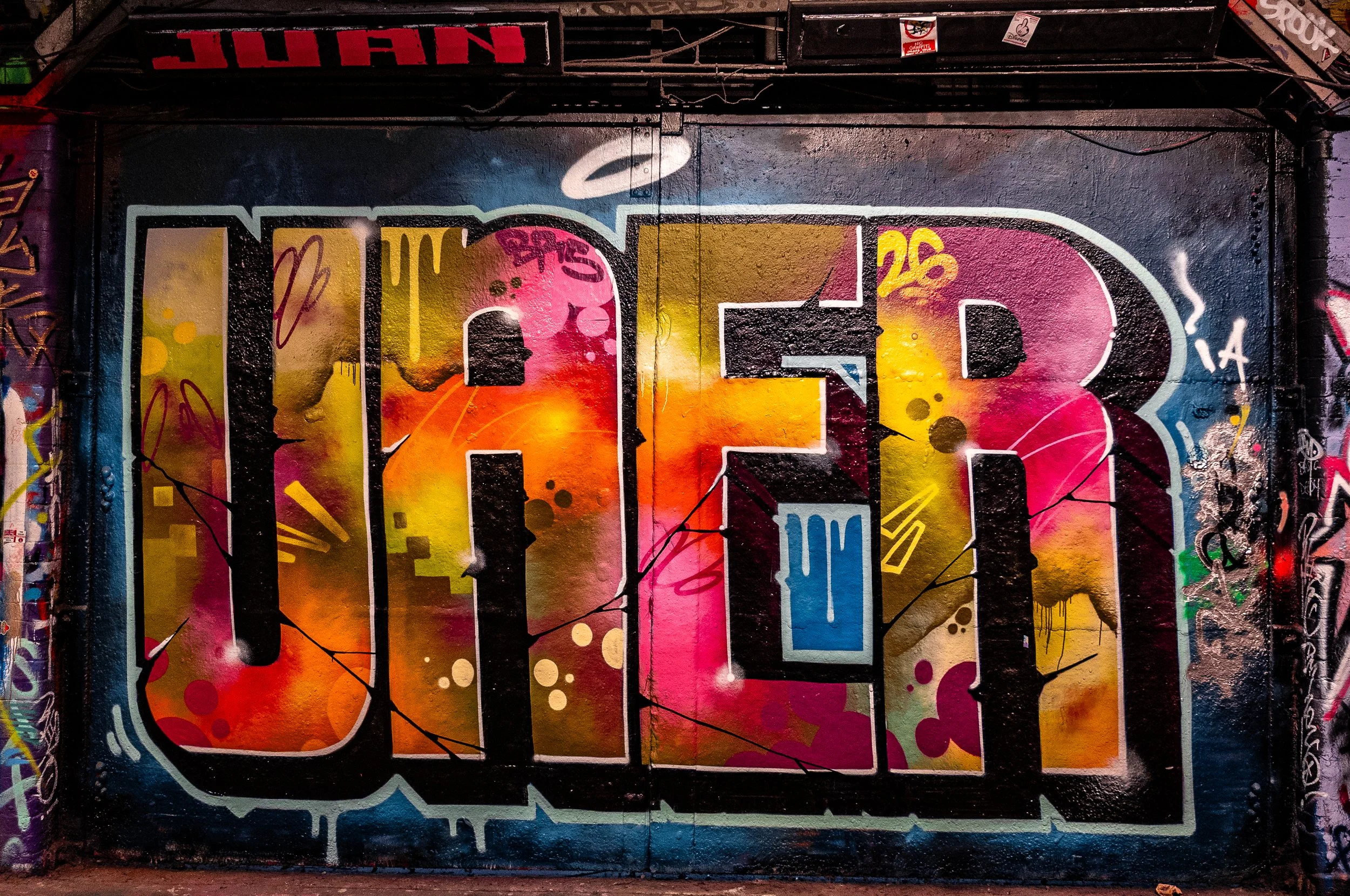 Colorful graffiti art on a brick wall with large, bold letters spelling 'CALI' filled with vibrant patterns and spray paint splashes.