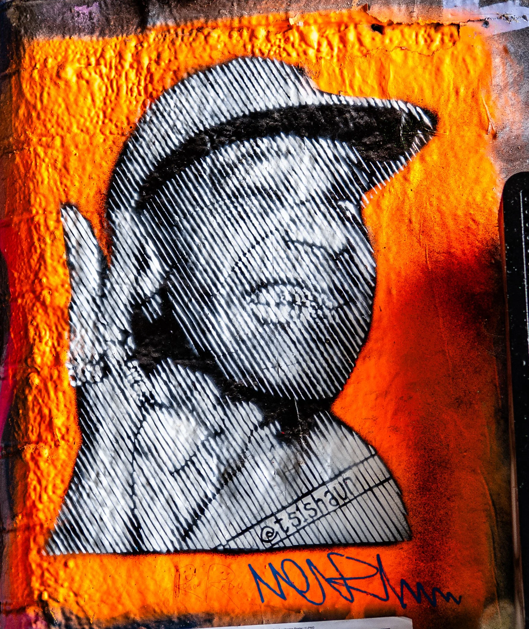 An orange street art painting of a woman with glasses, with black and white striped shading, signature, and social media handle