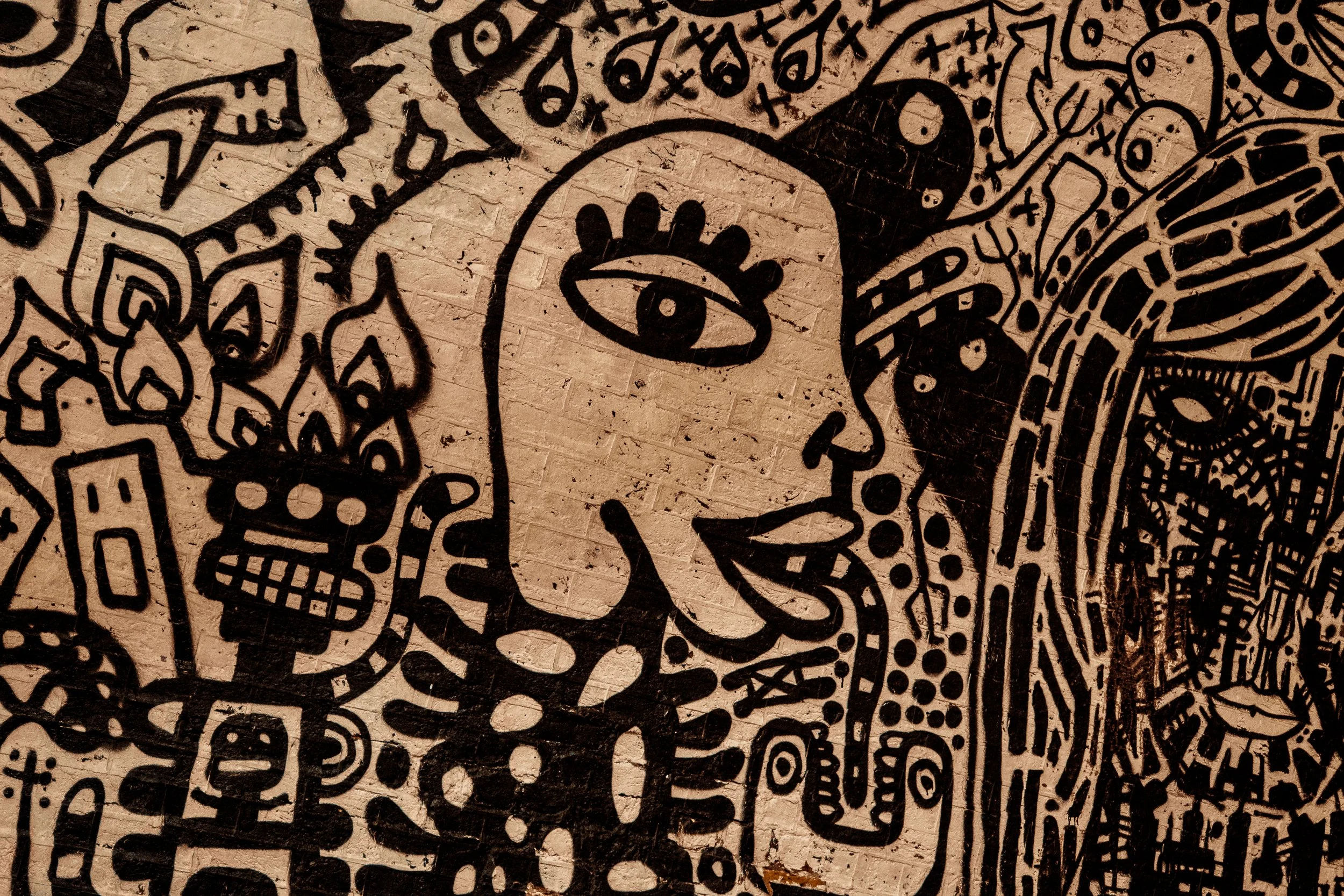 Black and white mural of a woman with an eye on her forehead, surrounded by abstract and skull designs on a brick wall.