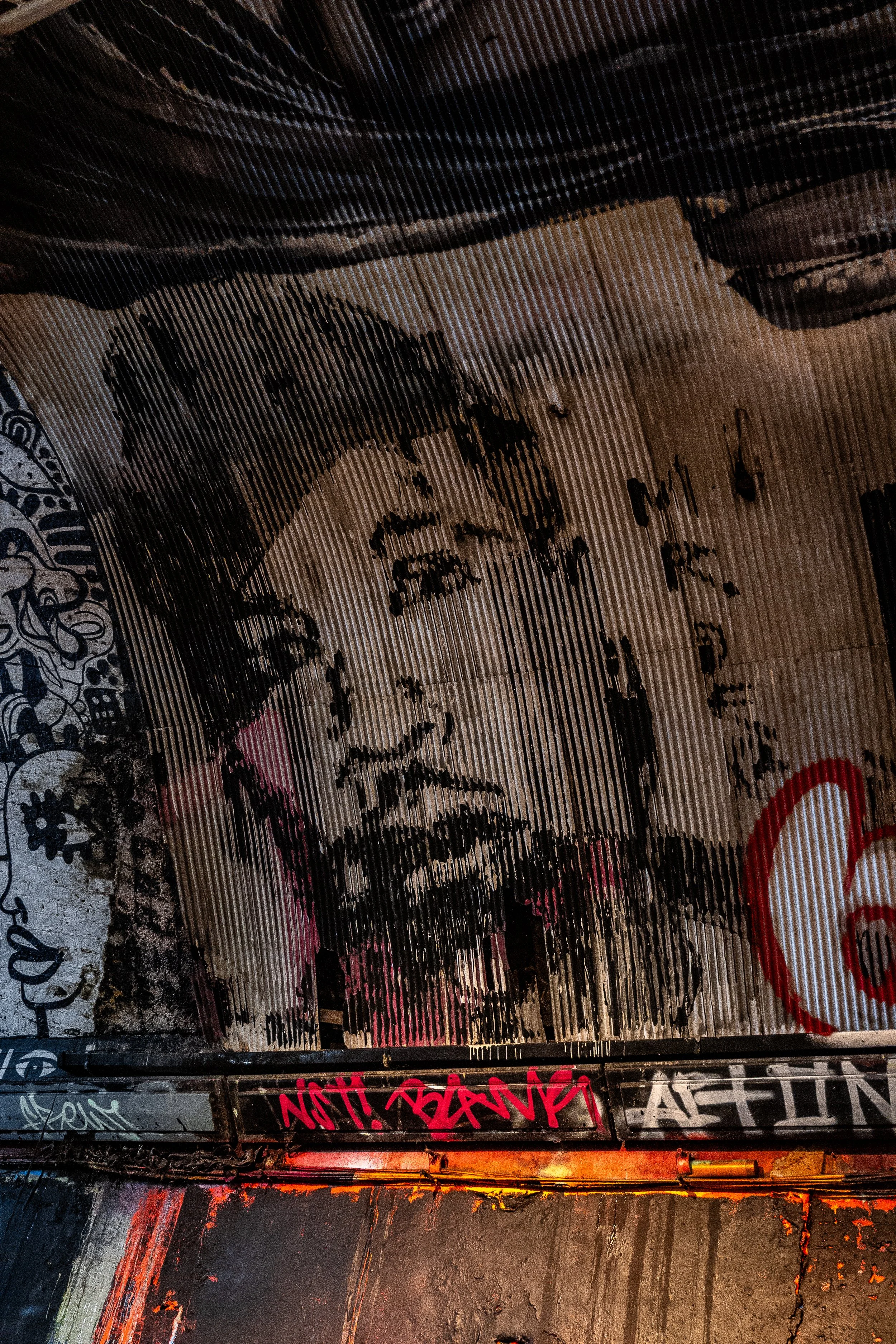 Street art mural of a woman's face with a pink highlight on her lips, black and white shading, graffiti tags around it, including a red spray-painted heart shape.