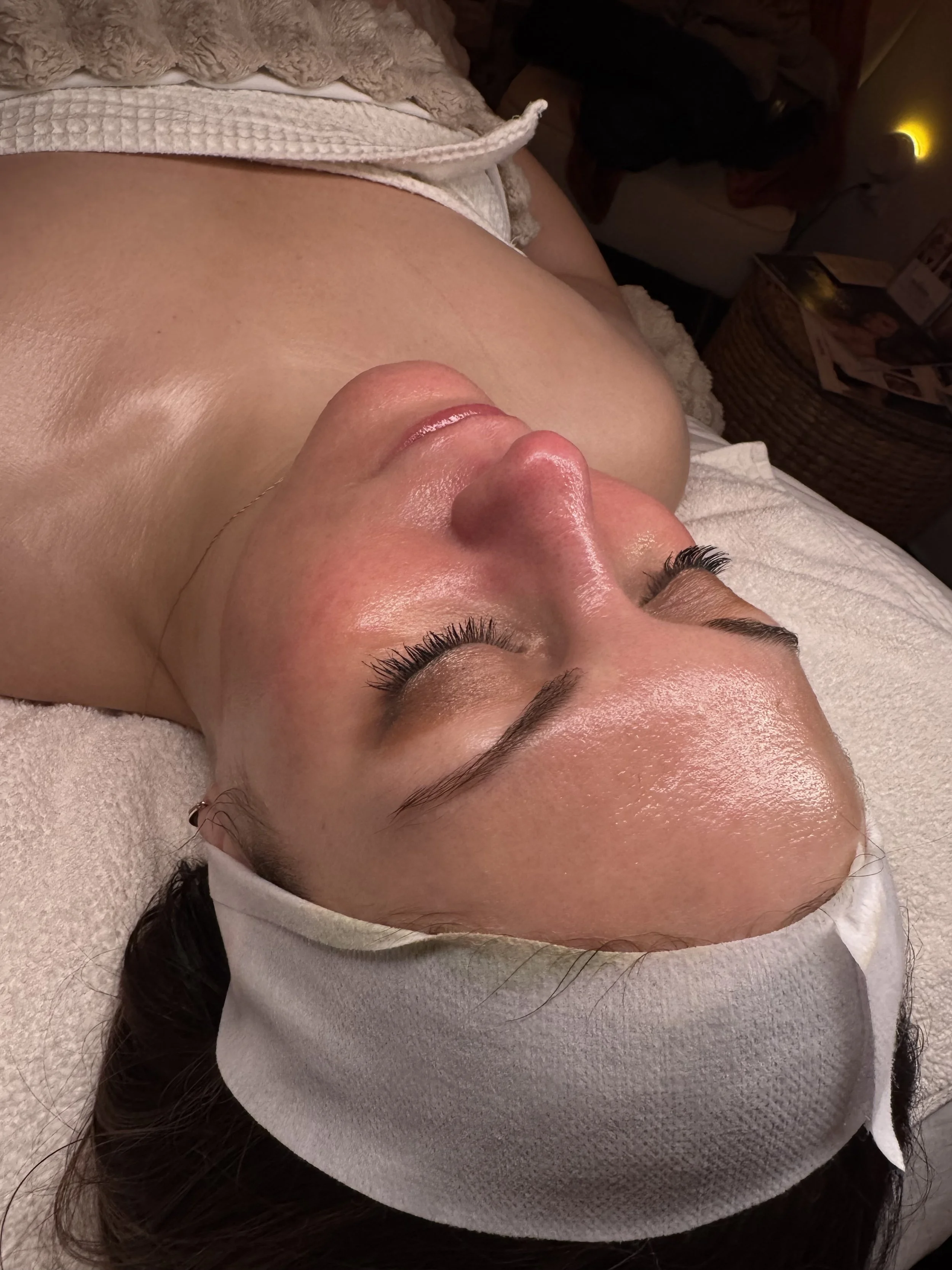 Person lying down with a spa headband, receiving a facial treatment, on a massage table.