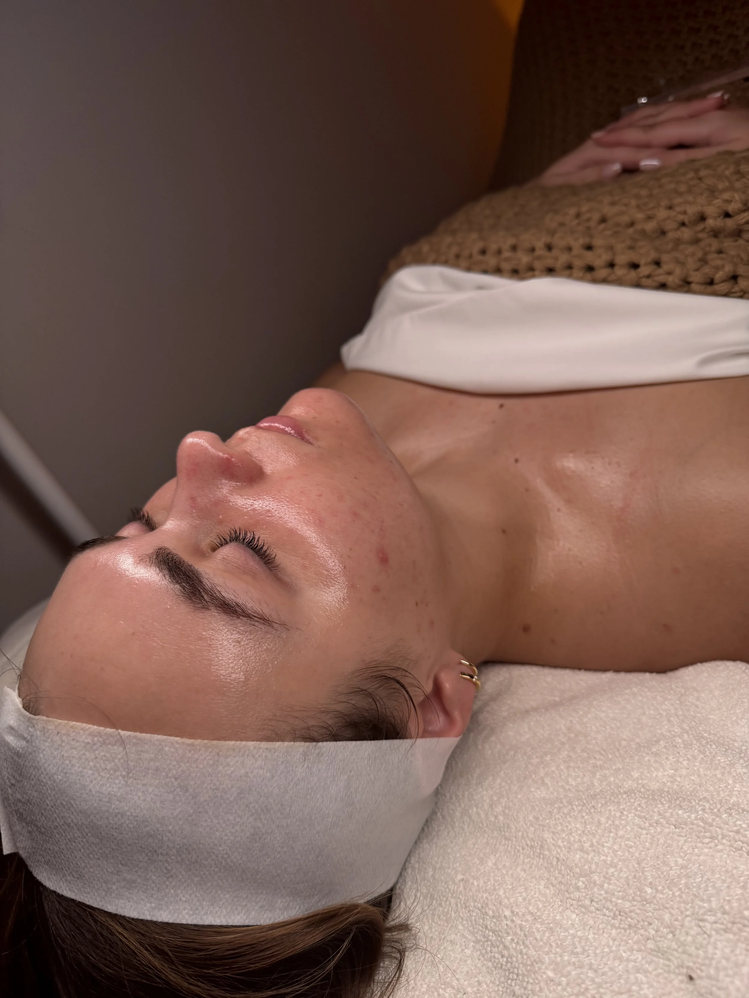 Person lying down with headband, receiving skincare treatment, wrapped in blanket, eyes closed, in spa setting.