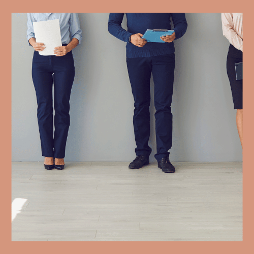 Three people standing in business attire, holding documents and tablets, with a minimal gray background.