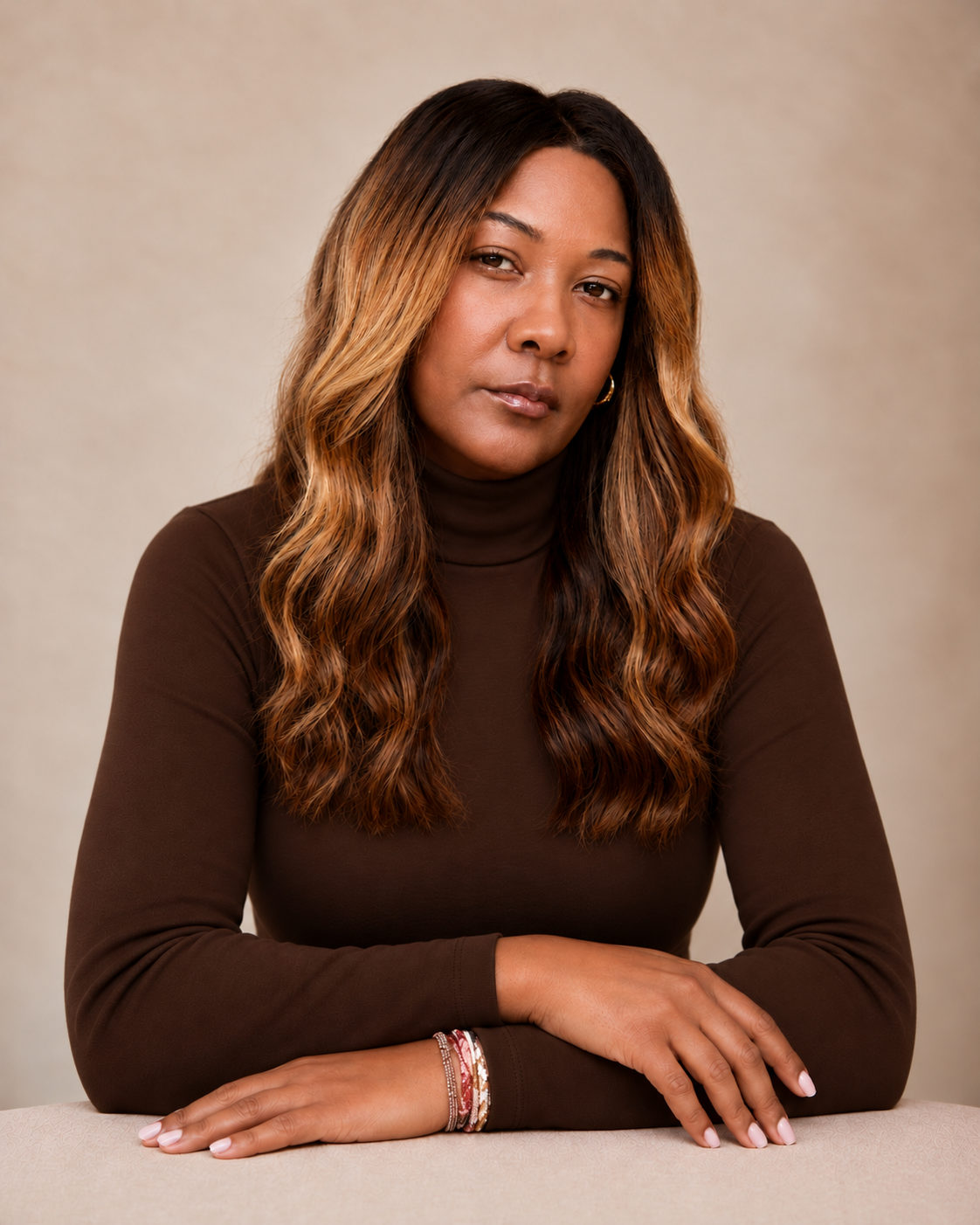 Geneèn Wright, workforce strategist and founder of Geneèn Wright HQ, in a brown turtleneck sweater against a warm beige background, arms crossed on ledge.