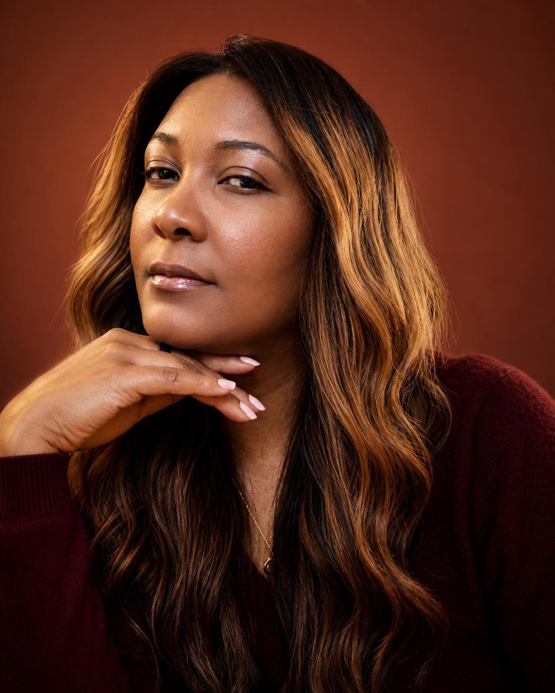 Geneèn Wright, workforce strategist and founder of Geneèn Wright HQ, in a burgundy sweater against a warm rust background, resting her chin on her hand.