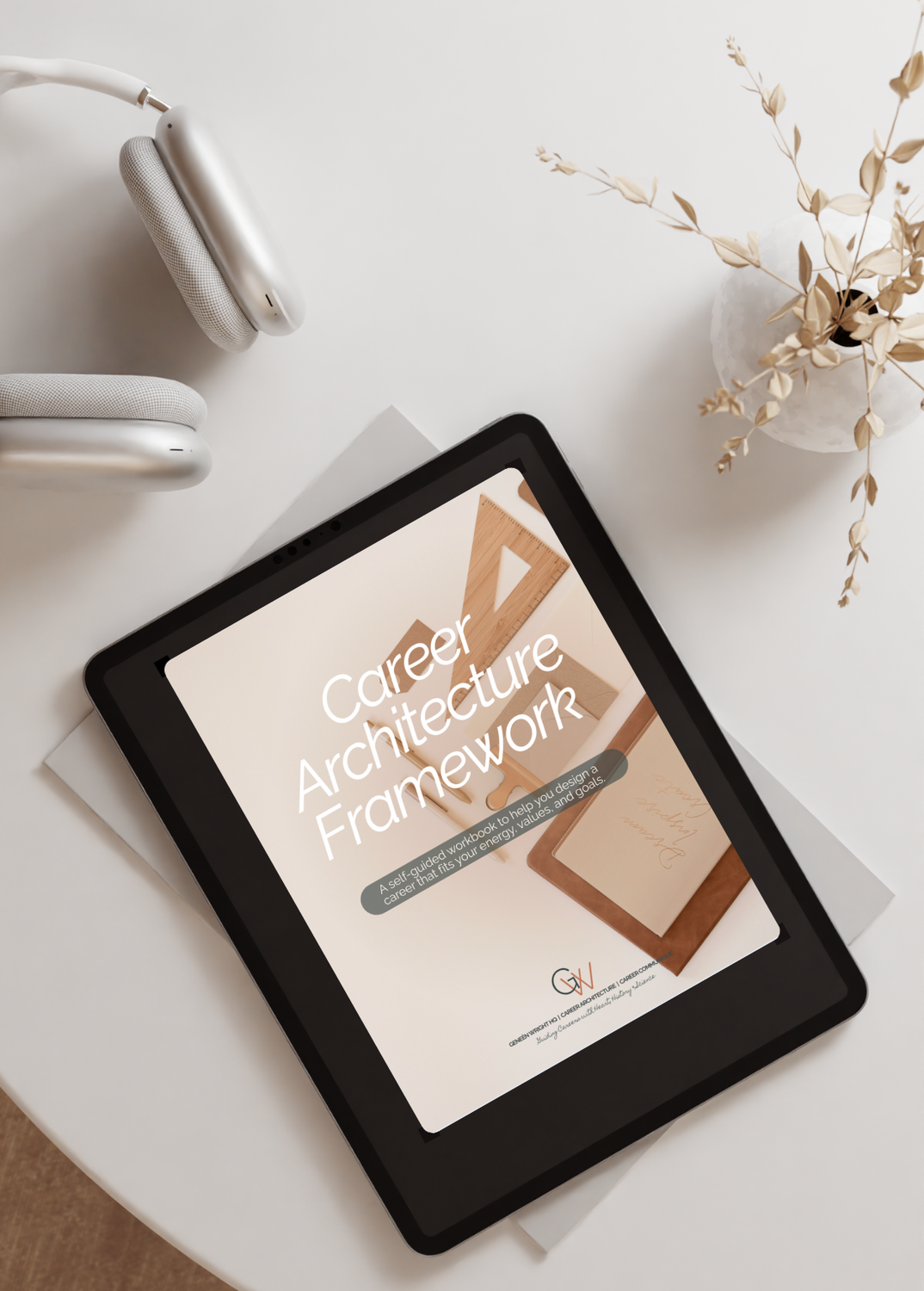 Tablet on a desk displaying a booklet titled 'Career Architecture Framework' with a subtitle about a self-guided workbook for designing a career aligned with energy, values, and goals, surrounded by a vase with dried flowers, a pair of white headphones, and some papers.