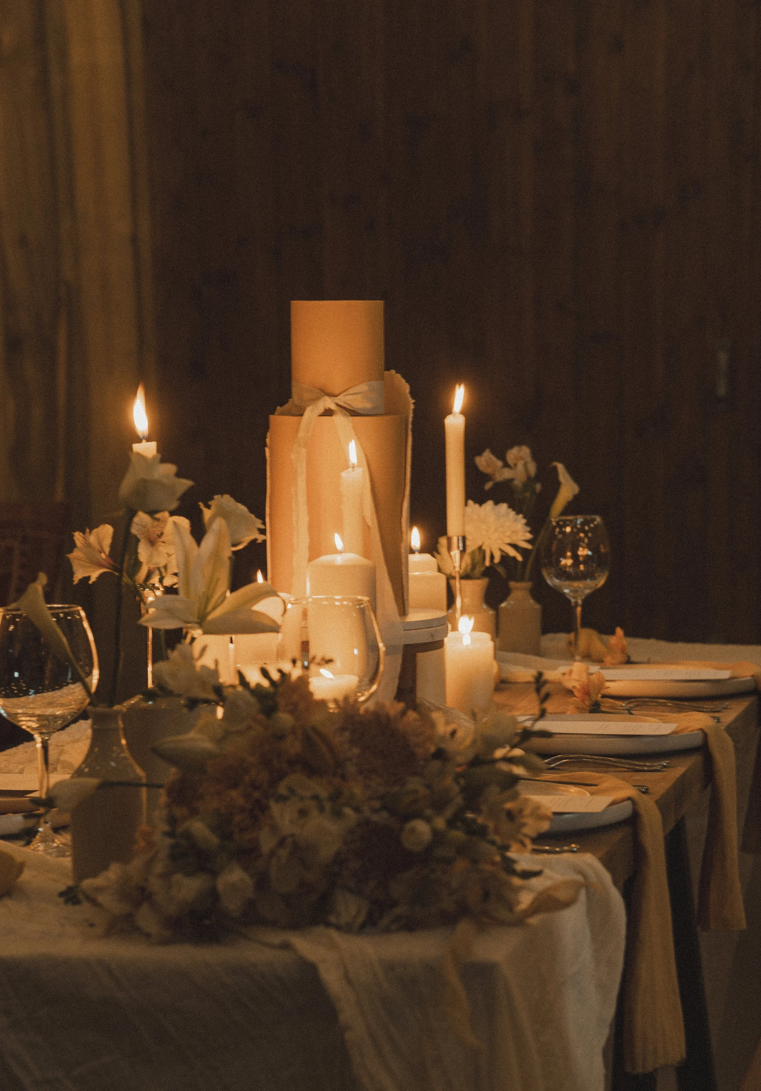 A decorated dinner table with lit candles, floral arrangements, wine glasses, and tableware in a warm, intimate setting.