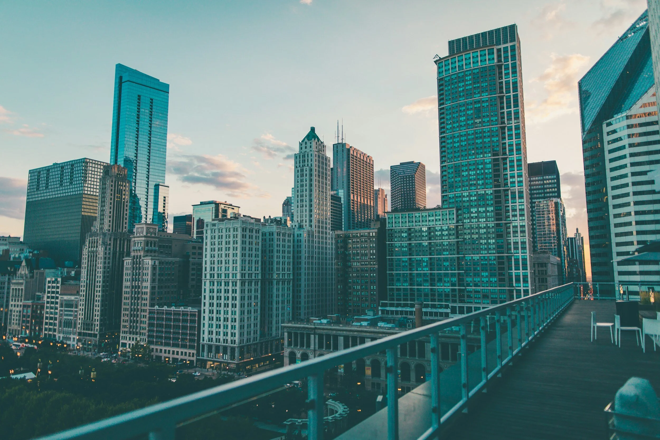 Chicago skyline viewed from a pedestrian bridge at sunset, featuring historic and modern skyscrapers.