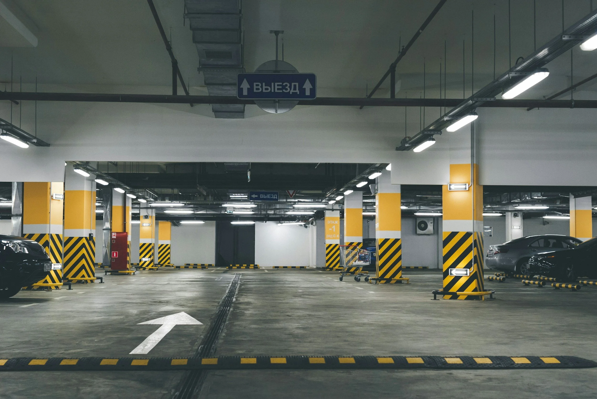 Underground parking garage with cars, yellow-and-black striped columns, directional arrows, and Russian exit signs.