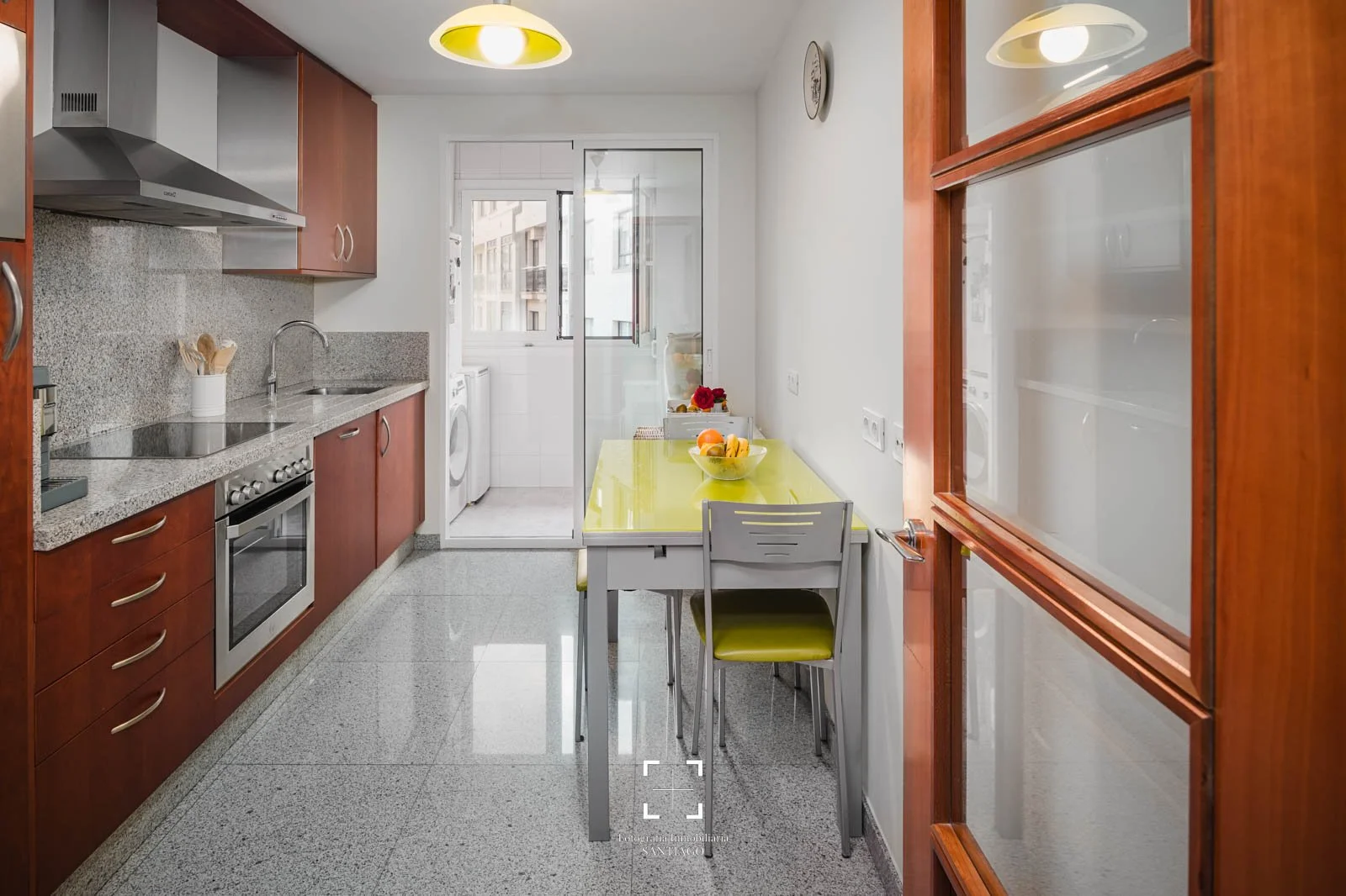 Fotografia Interiores, Fotografo Airbnb, Foto hotel. Cocina con gabinetes de madera, encimera de granito, electrodomésticos, mesa con sillas y puerta a lavandería con ventana