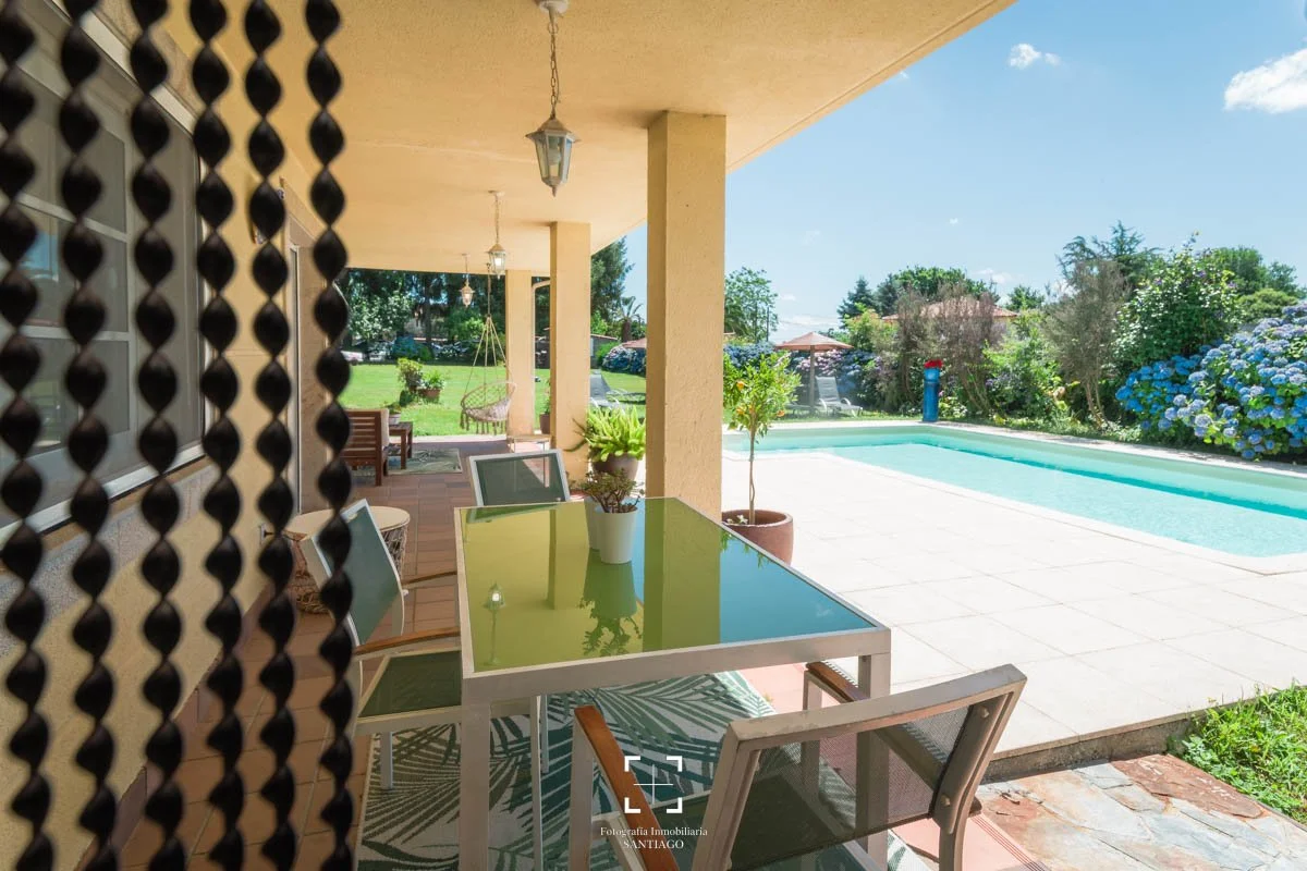 Vista de un patio con piscina, muebles de exterior, plantas y áreas verdes bajo un cielo despejado.
