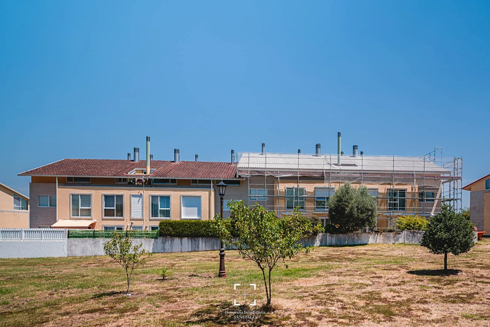Construcción de un edificio residencial con andamios y árboles en primer plano. Fotografía profesional de obra para empresa constructora