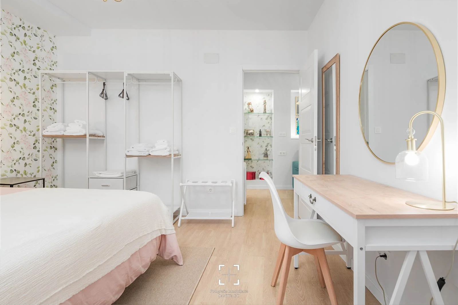 Habitación con cama, espejo redondo en la pared, escritorio con silla, lámpara y estantería con decoraciones.