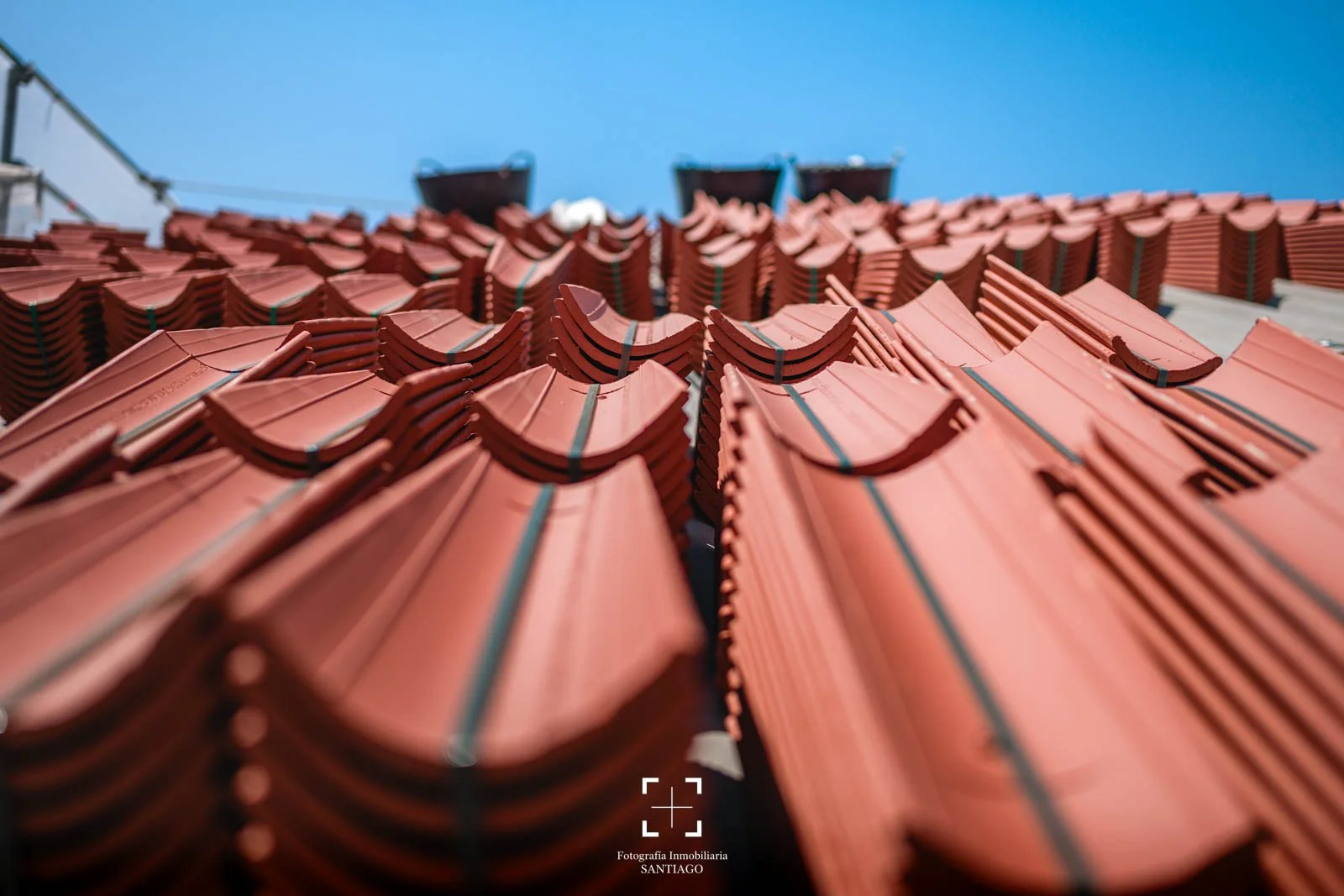 Lote de tejas rojas apiladas para construcción, vista de abajo hacia arriba con cielo azul y estructuras en el fondo. fotografia comercial y negocios
