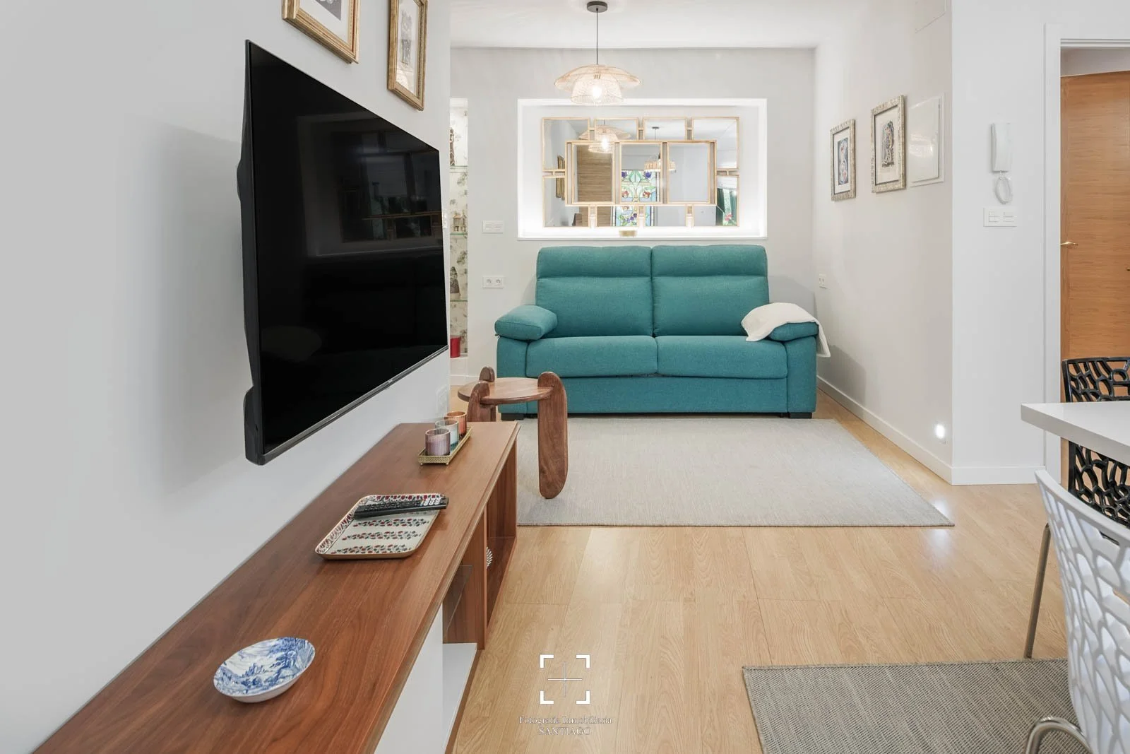 Sala de estar con sillón azul, televisor en la pared, mesa de madera con objetos decorativos y cuadros en la pared