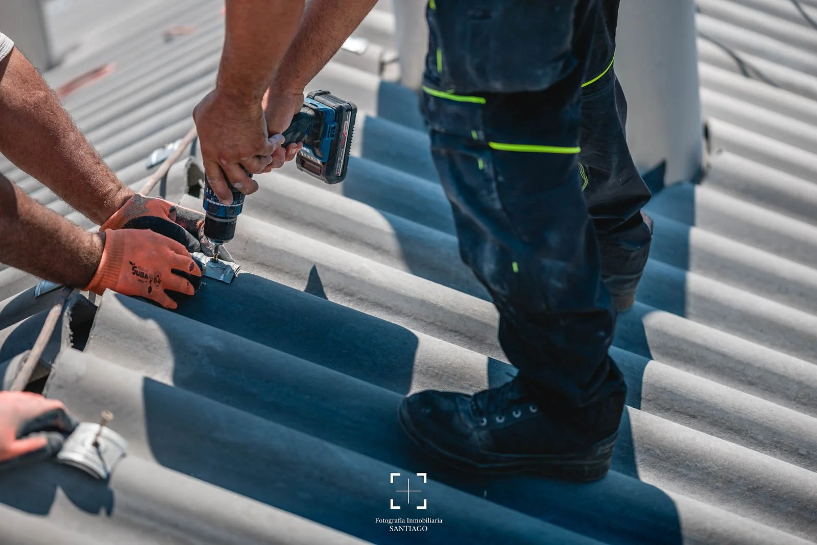 Personas instalando láminas de metal en un techo con herramientas eléctricas, usando guantes y ropa de trabajo. fotografia comercial y negocios