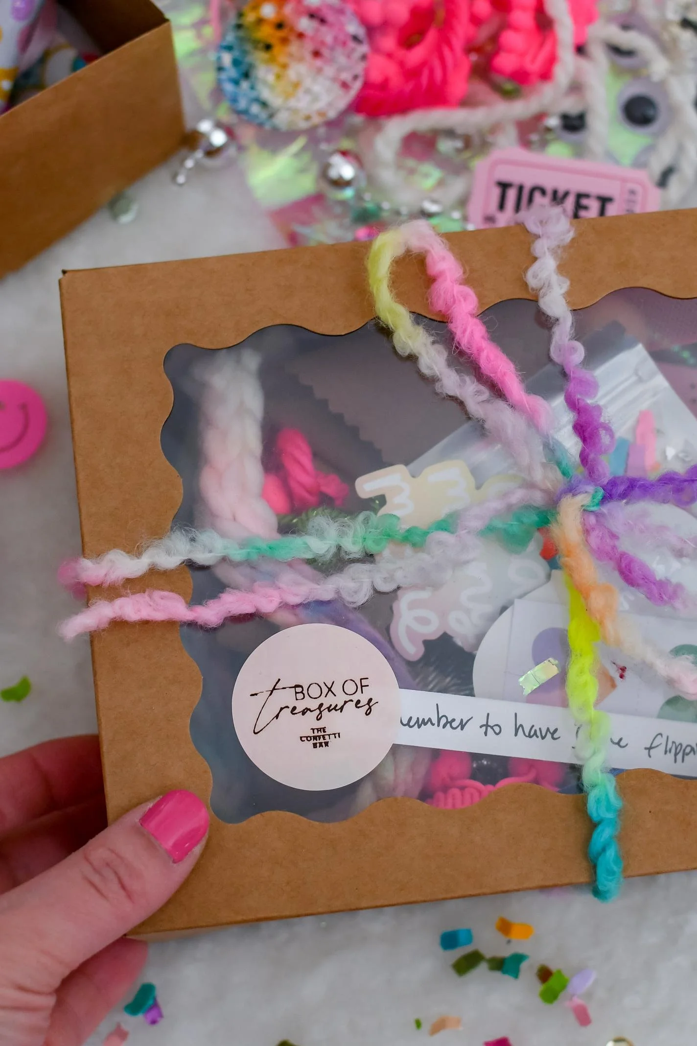 Kraft box tied with colorful ribbon, filled with an assortment of colorful craft items.