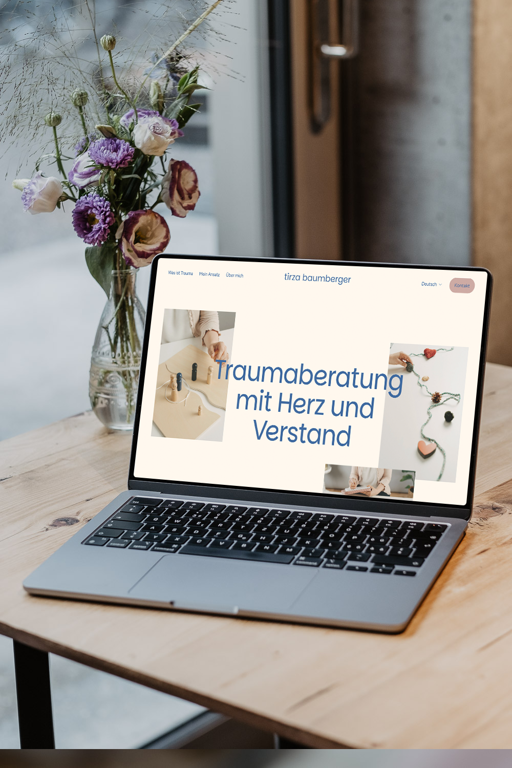 Ein Laptop auf einem Holztisch zeigt eine Webseite für Traumberatung. Neben dem Laptop steht eine Glaskaraffe mit bunten Blumen. Im Hintergrund befindet sich eine Tür.