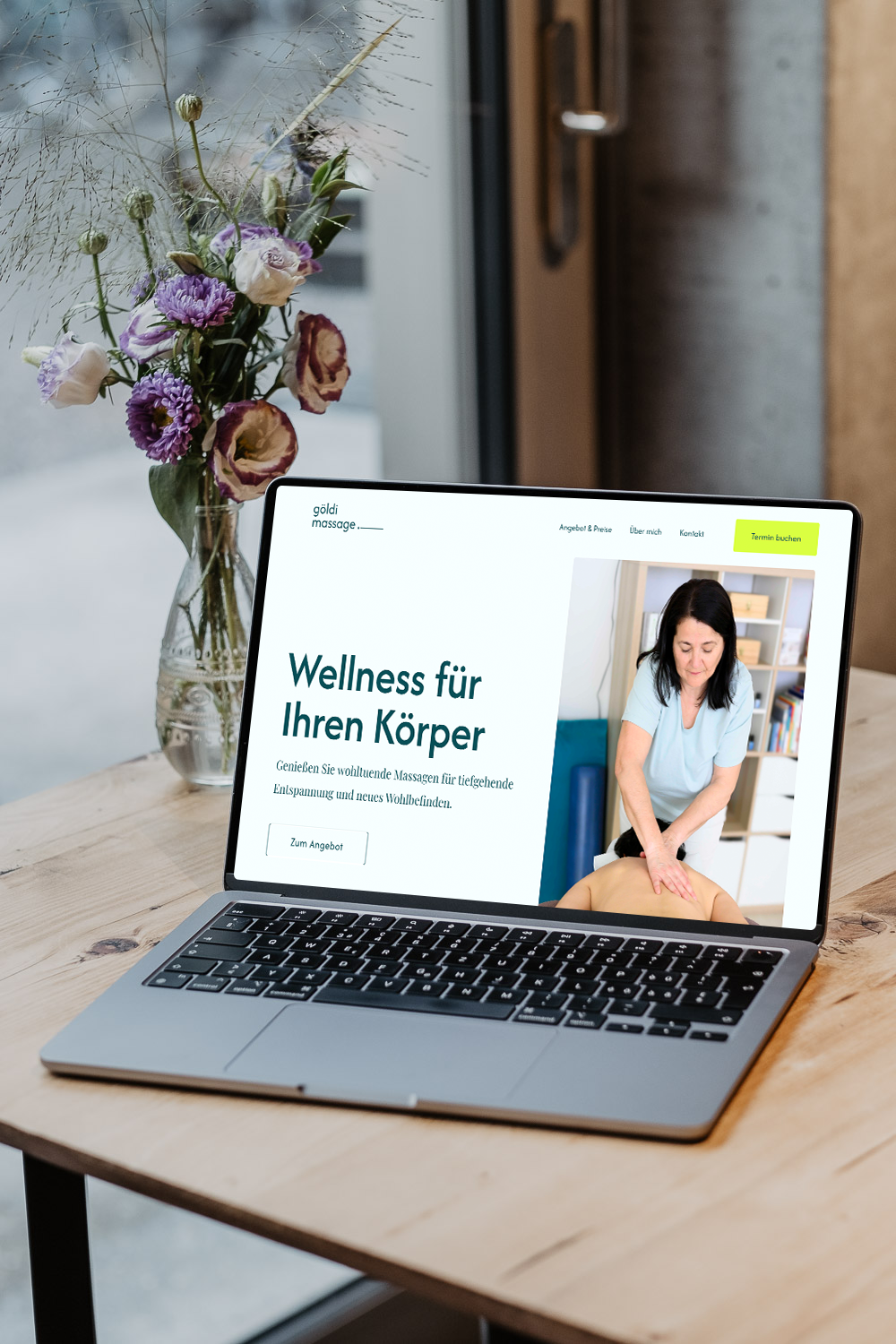 Laptop auf einem Holztisch mit einer Webseite für Wellnessbehandlungen. Neben dem Laptop steht eine Vase mit bunten Frühlingsblumen.