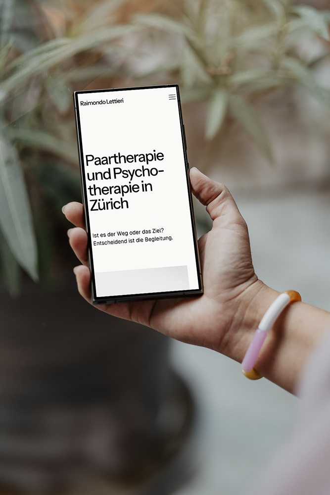 Hand hält Smartphone mit Website über Paartherapie und Psycho­therapie in Zürich, im Hintergrund Pflanzen