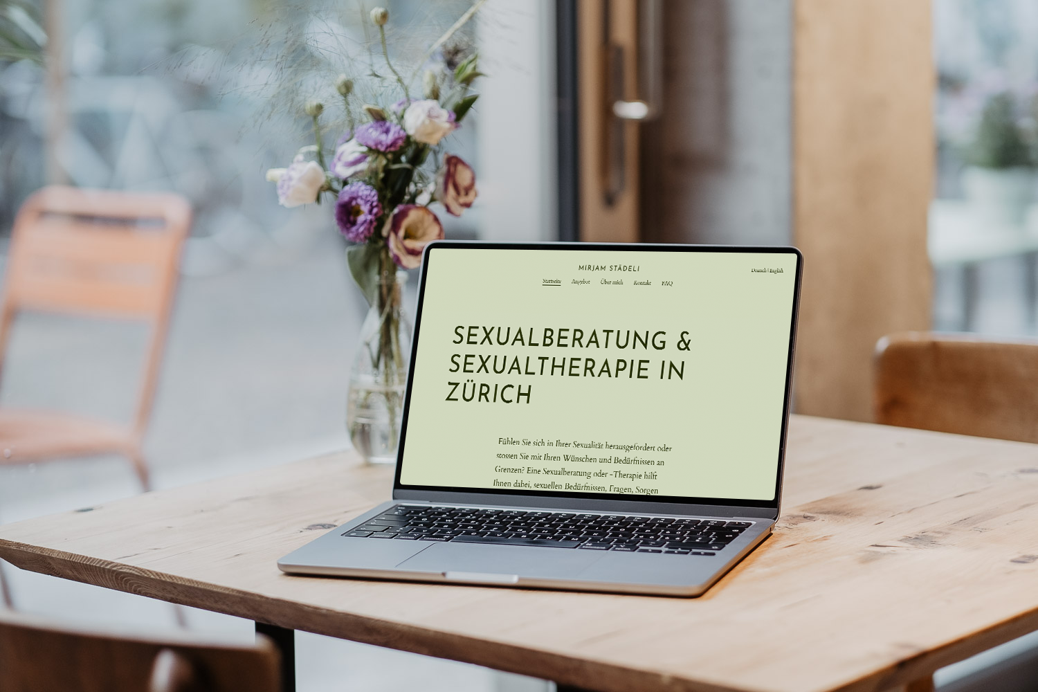 Ein Laptop zeigt eine Website über Sexualberatung und Sexualtherapie in Zürich auf einem Holztisch neben einem Blumenstrauß in einer Vase.