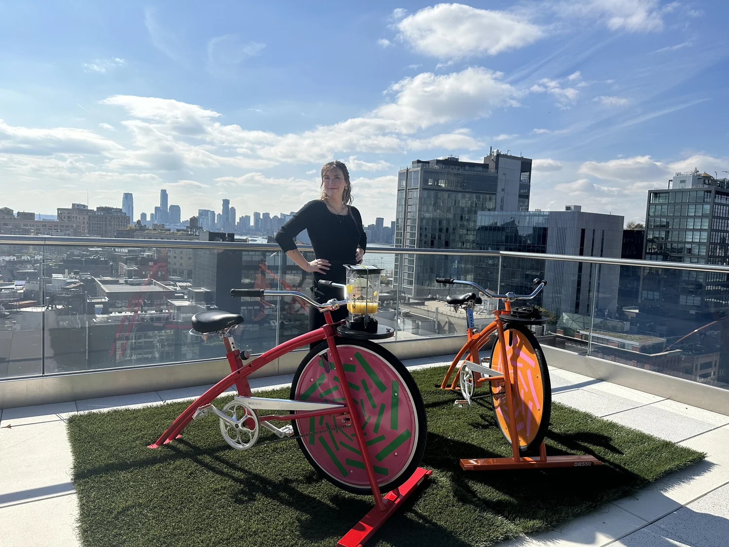 Two colorful smoothie bikes set up on a rooftop with a city skyline