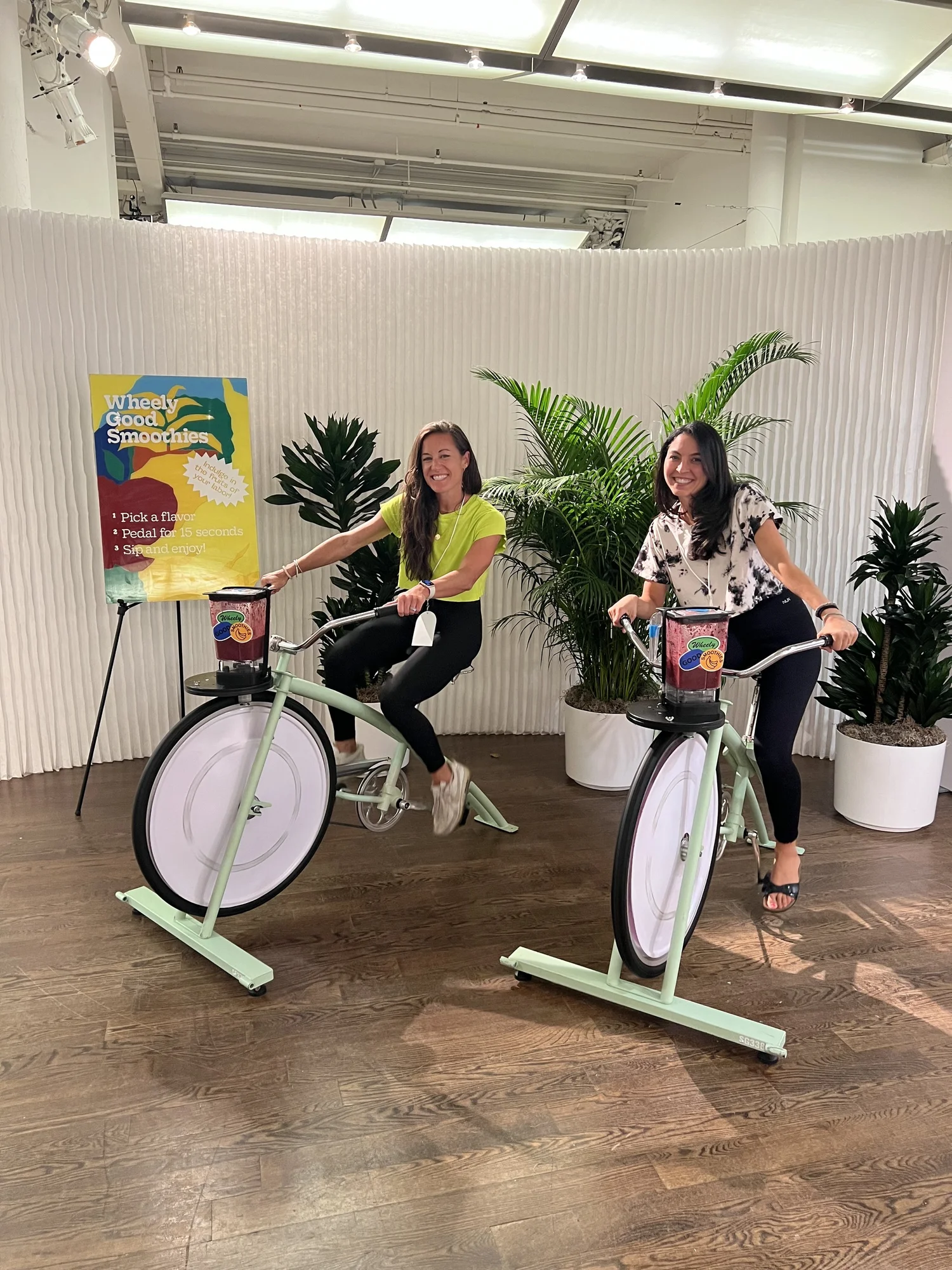 Two guests smiling while pedaling smoothie bikes at a Wheely Good Smoothies event