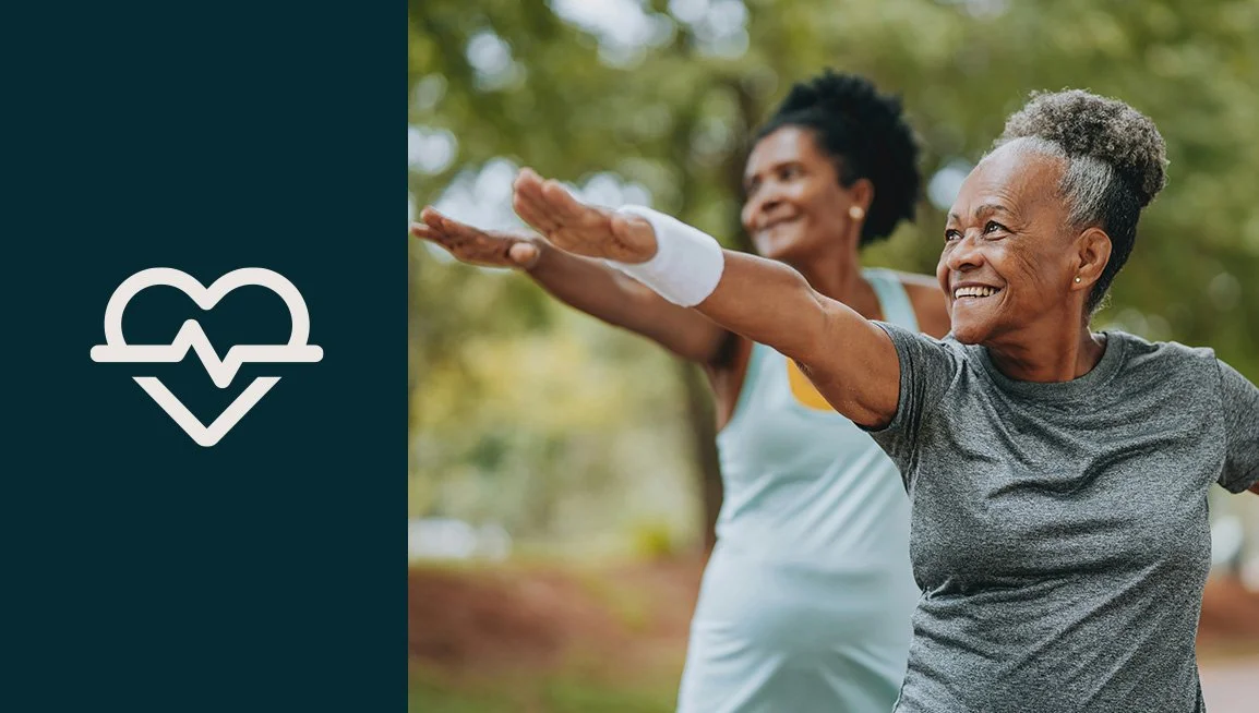 Two elderly women exercising outdoors, stretching their arms out and smiling, with a green, leaf-filled background.