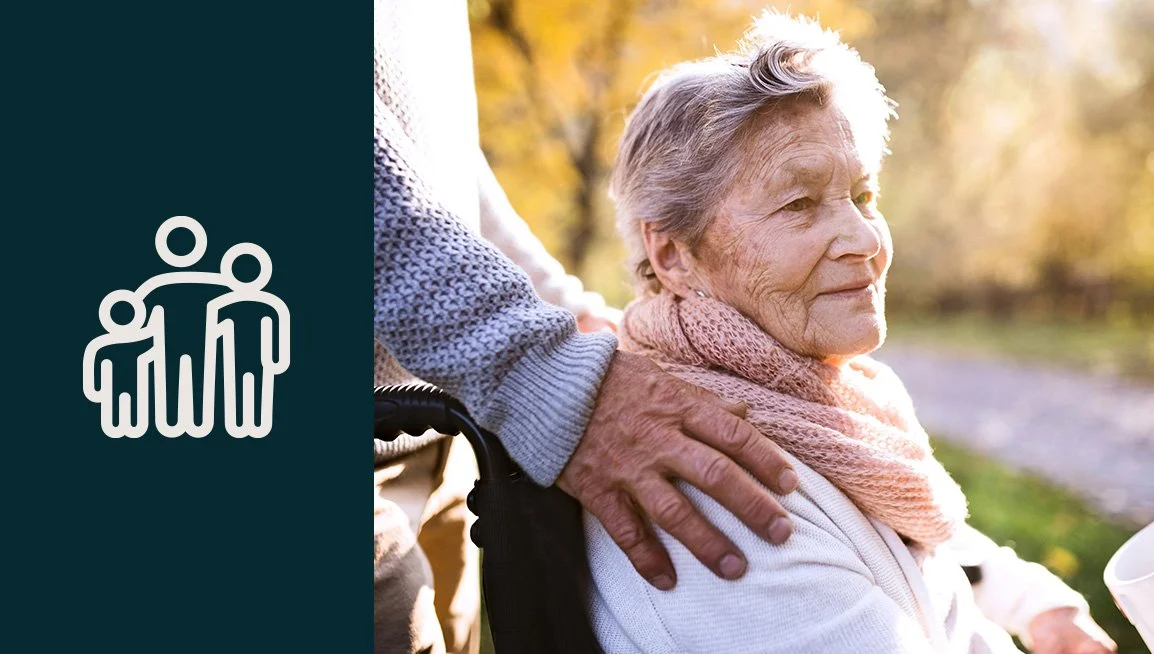 An elderly woman sitting outdoors in warm clothing with sunlight in the background, being gently supported by a caregiver.