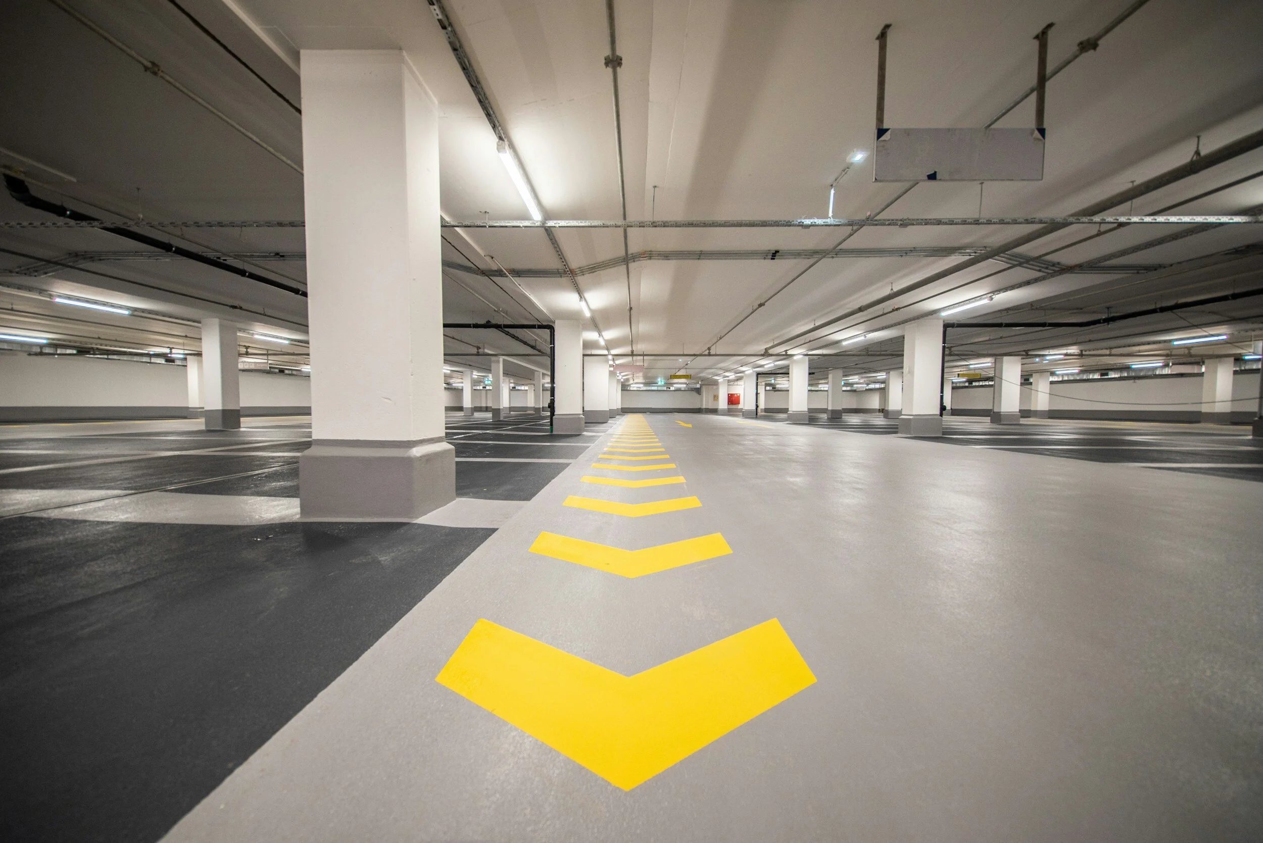 Empty underground parking garage with yellow directional arrows painted on the concrete floor.