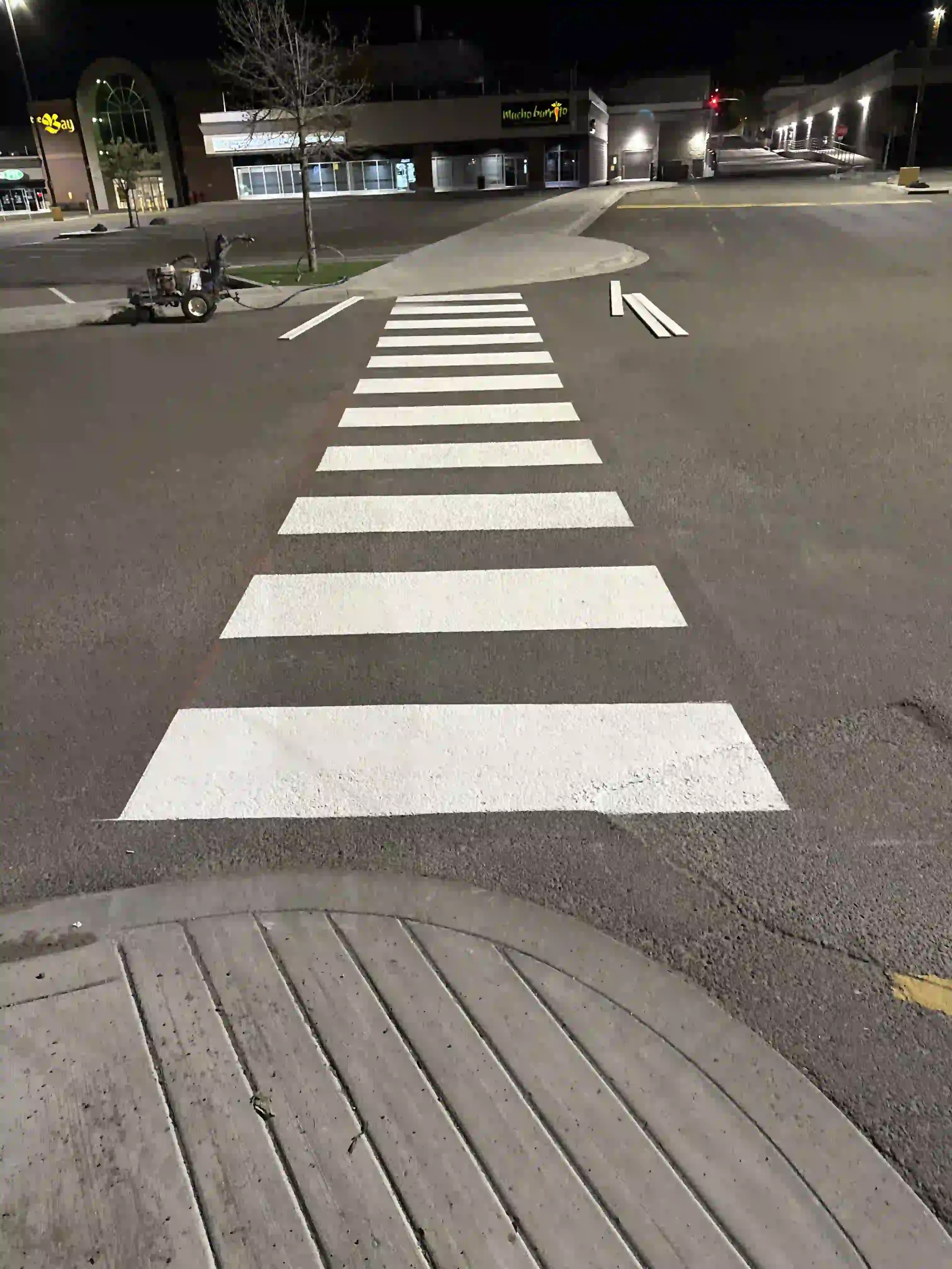 An Epic Pavement line painting machine applying fresh white pedestrian crosswalk markings in a commercial shopping plaza.