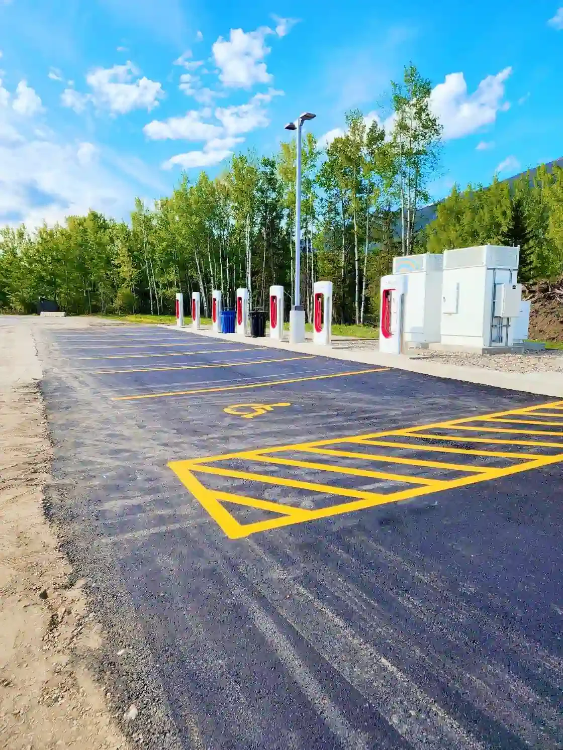 Tesla Supercharger station parking lot in McBride, BC, with freshly painted yellow accessible parking markings and hatched access aisle by Epic Pavement