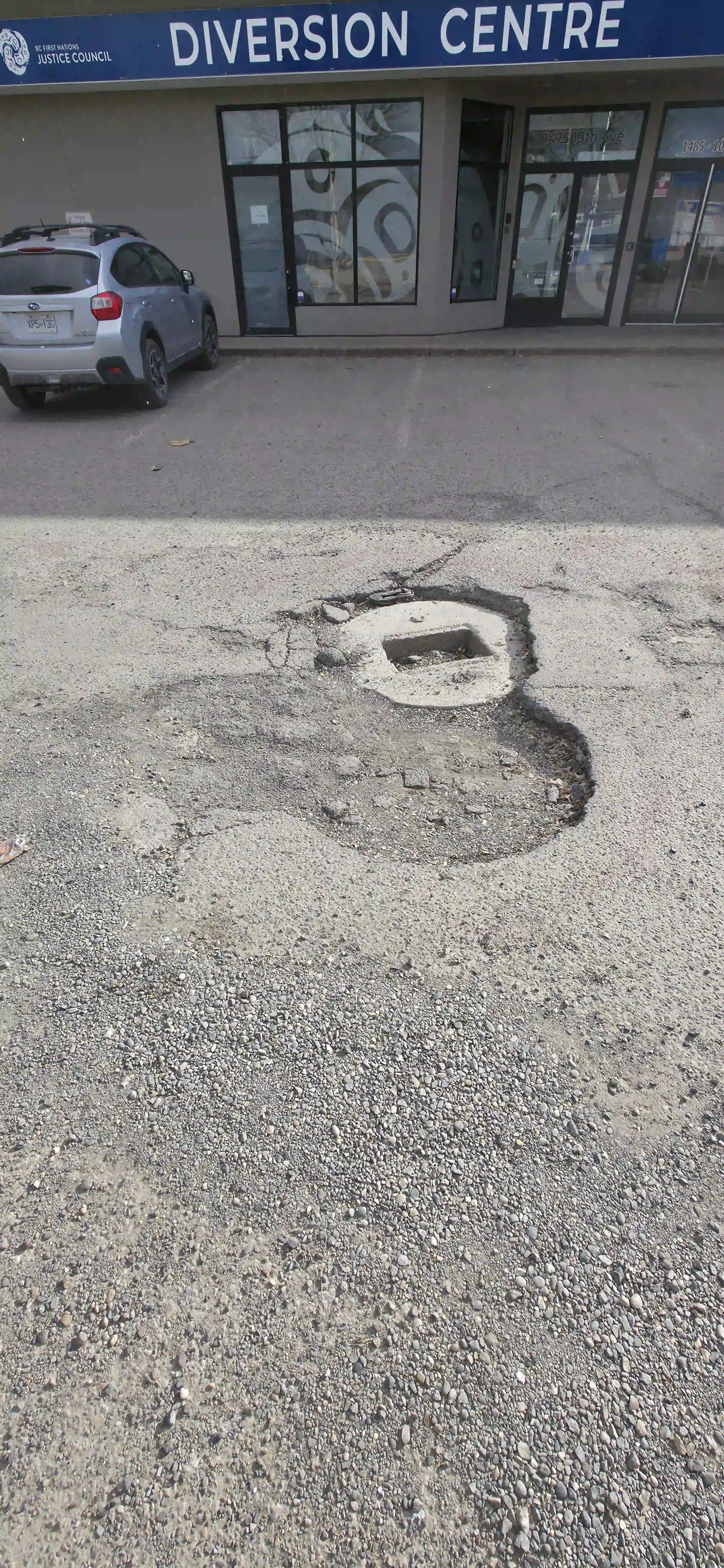 Severe asphalt damage and a large pothole surrounding a catch basin in a commercial parking lot in Prince George, prior to repair.
