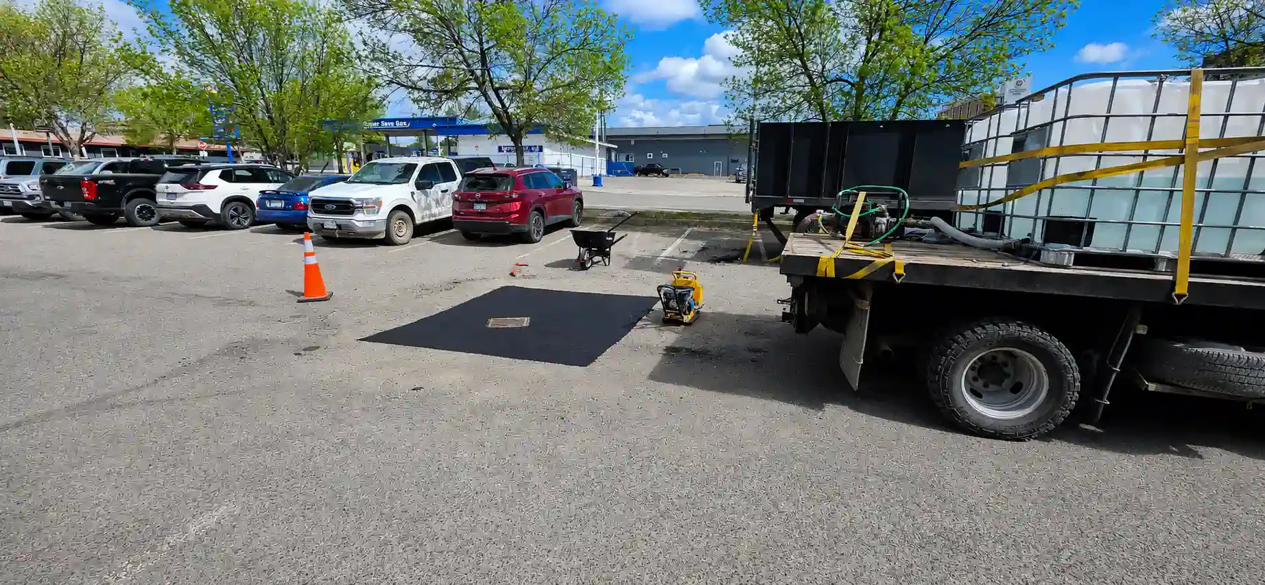 An Epic Pavement work site prepared for catch basin restoration, showing a precisely cut asphalt square, a walk-behind plate compactor, and a work truck.